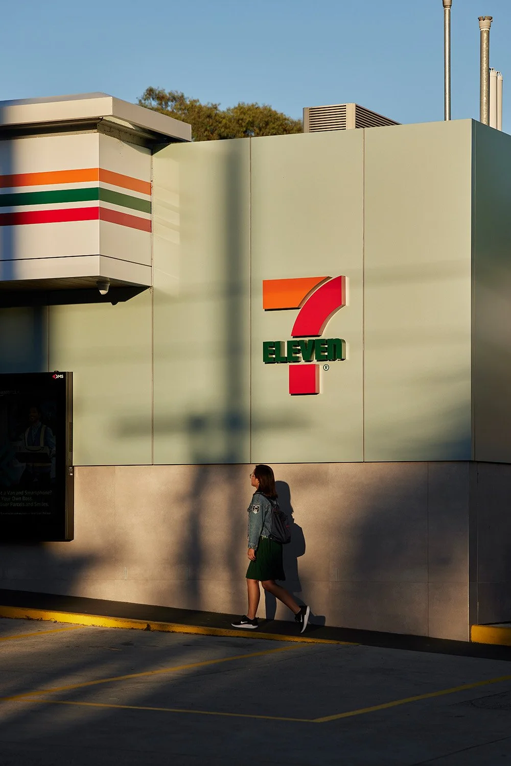 A woman walking past a 7-Eleven store with the store's logo on the wall.
