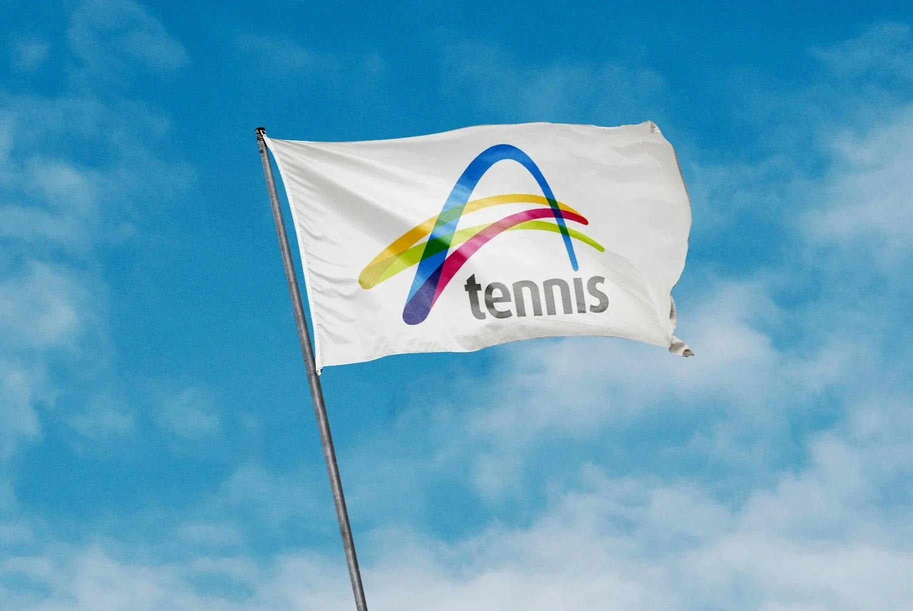 A white flag with a colorful, stylized tennis logo and the word "tennis" written in gray, waving in the sky with some clouds in the background.