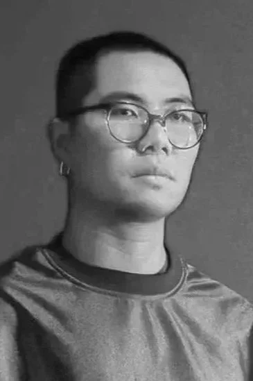 Black and white portrait of a woman with short hair, glasses, and a calm expression, wearing a t-shirt.