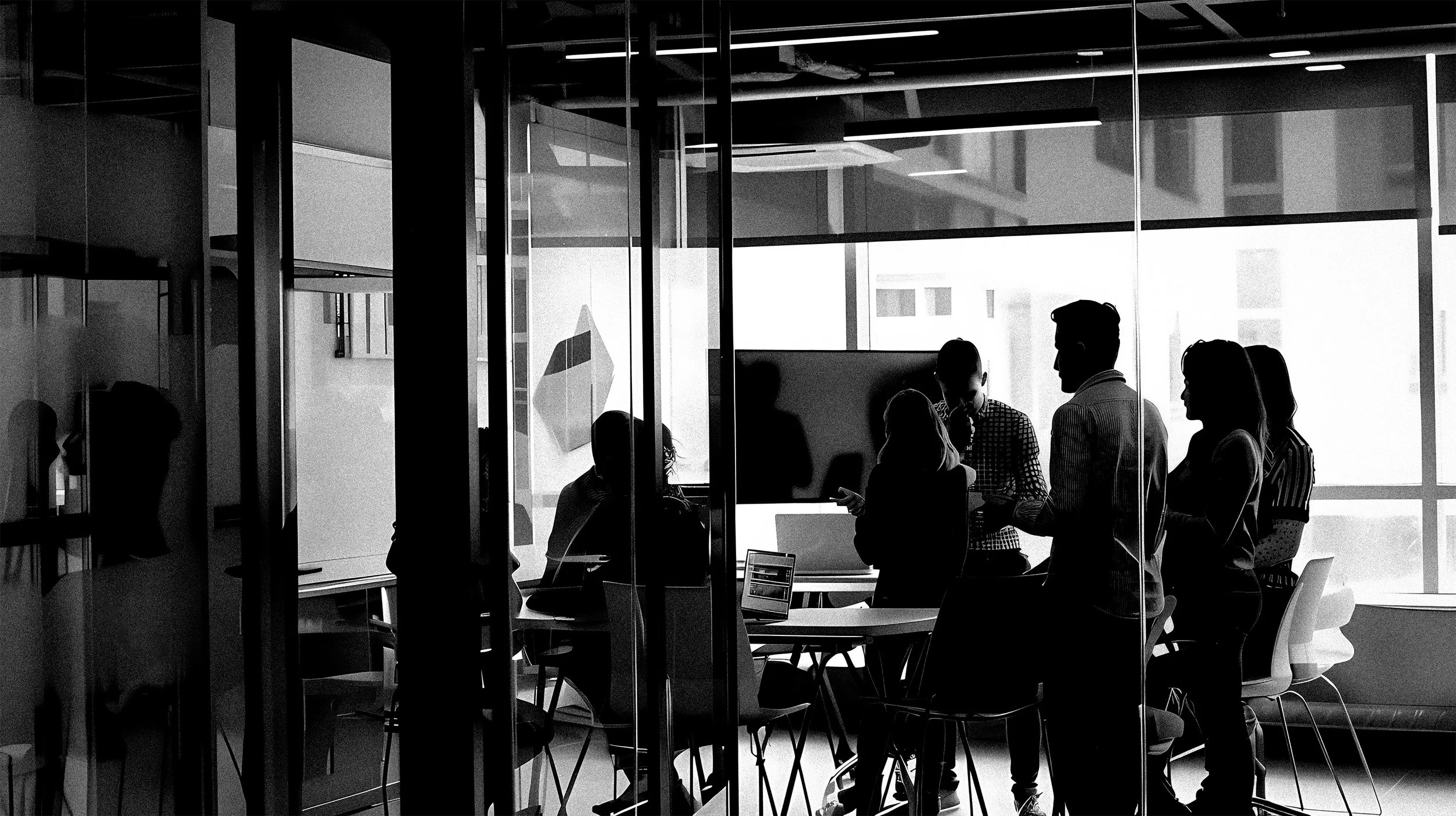 Silhouettes of people gathered in a modern office conference room with large windows, working and talking.