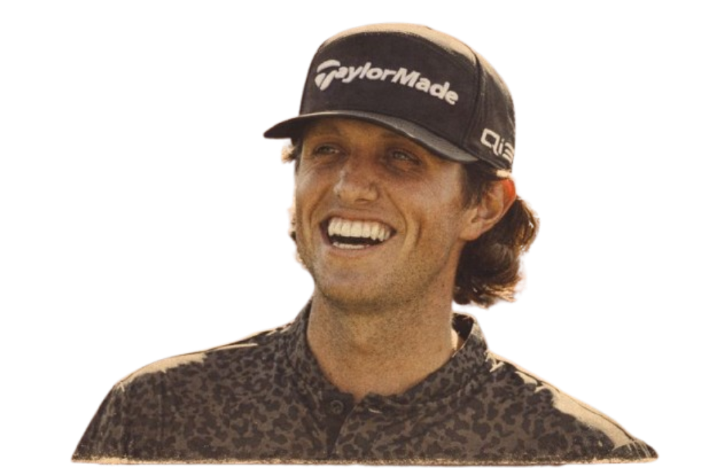 A man with shoulder-length hair wearing a black TaylorMade cap and a leopard-print shirt, smiling and looking to the side.