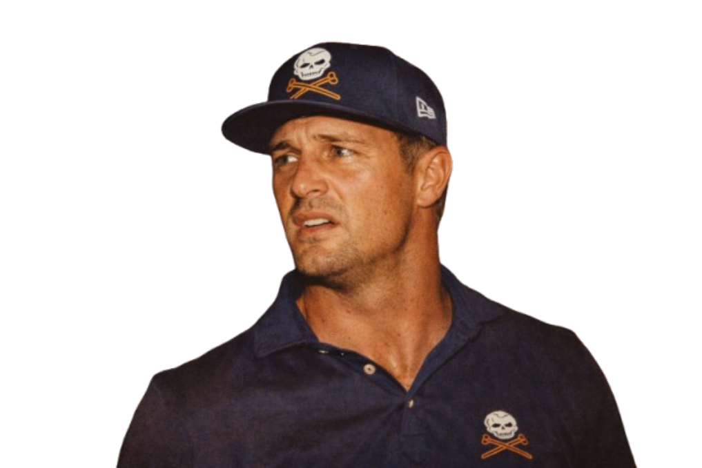 A man wearing a navy blue cap with a skull and crossbones logo and a navy polo shirt with a matching logo, looking to his right with a confused or skeptical expression.