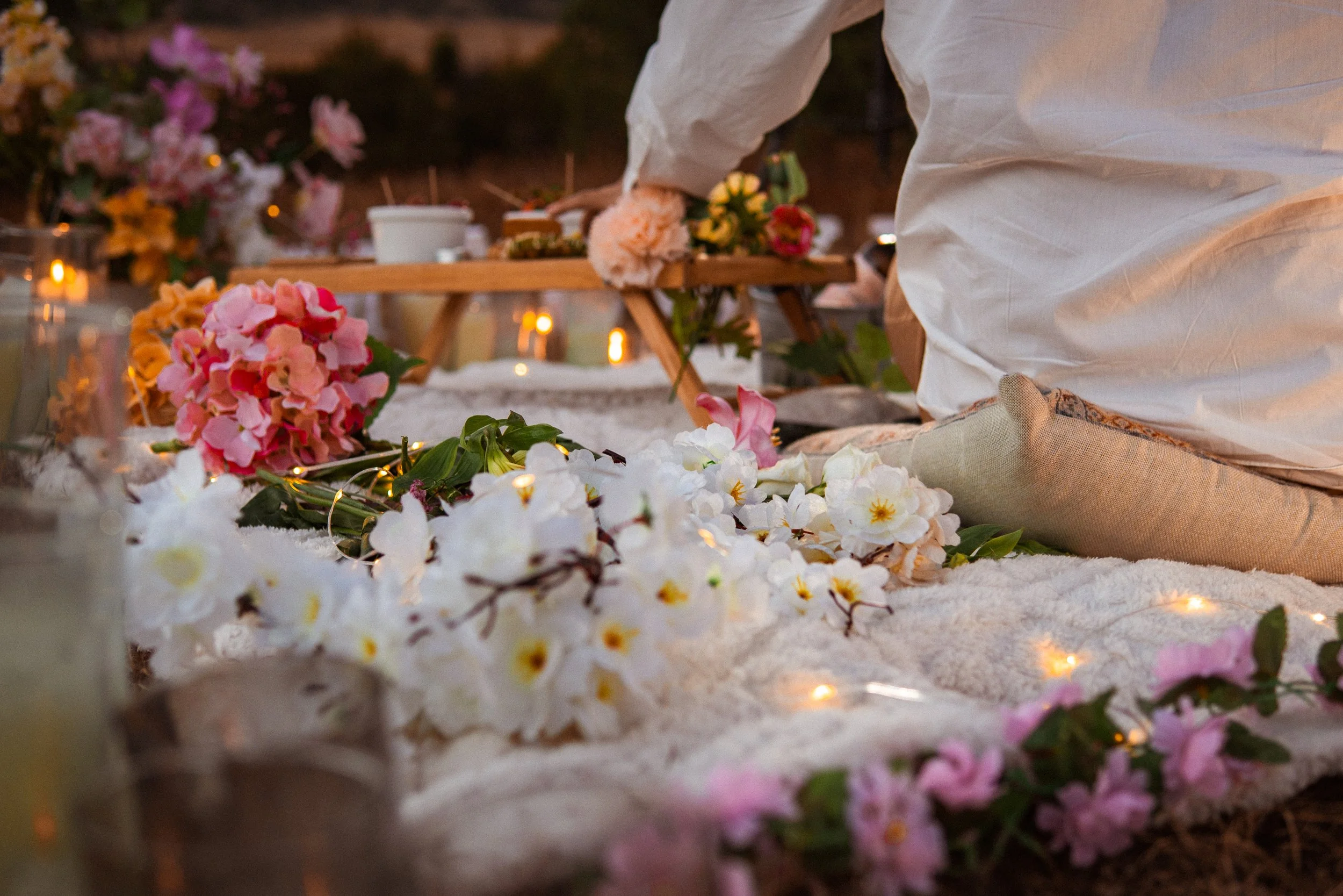 Persona en posición de rodillas en un altar decorado con flores y velas, participando en una ceremonia o ritual al aire libre en un ambiente íntimo y floral.