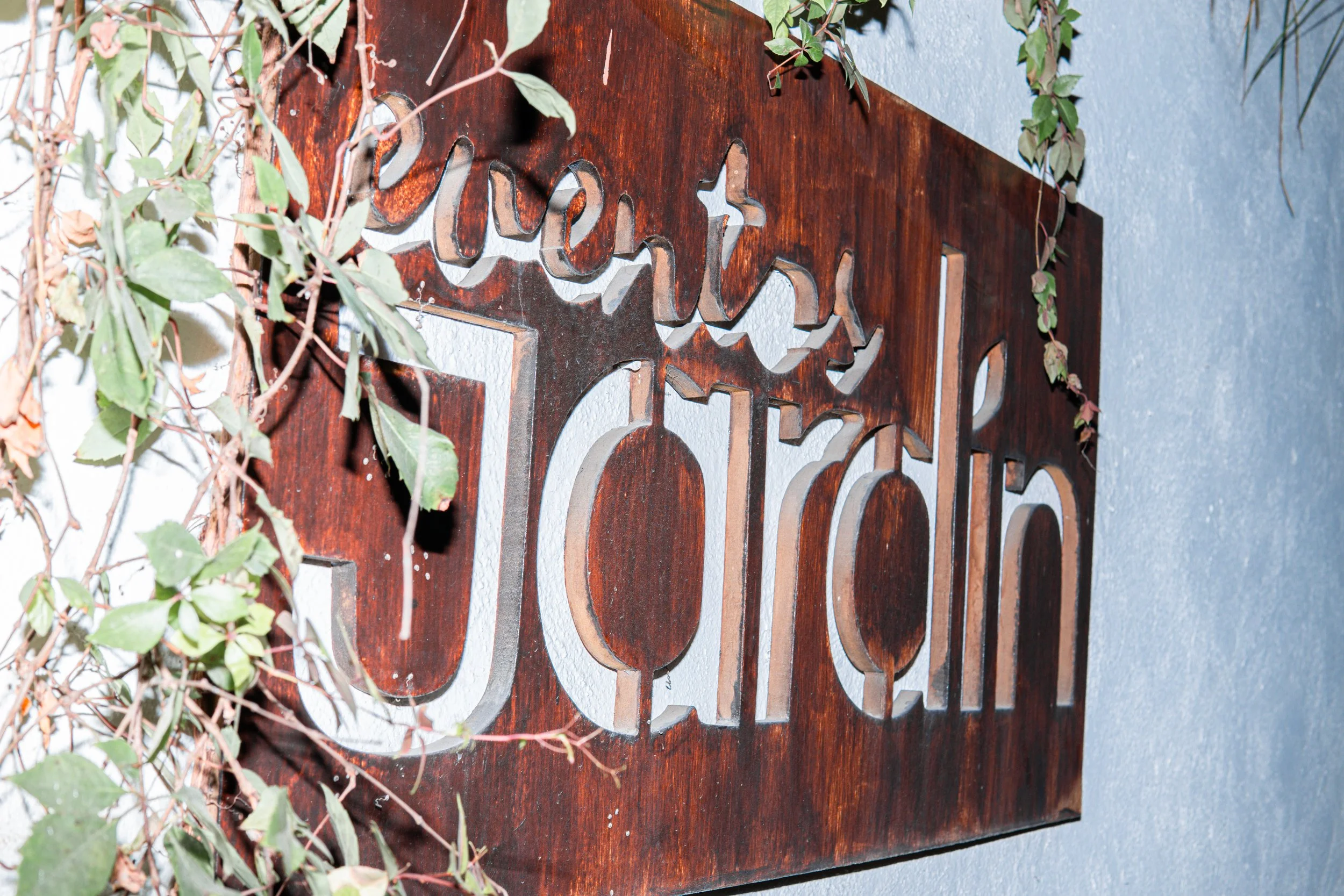 Cartel de madera con letras recortadas, decorado con plantas verdes