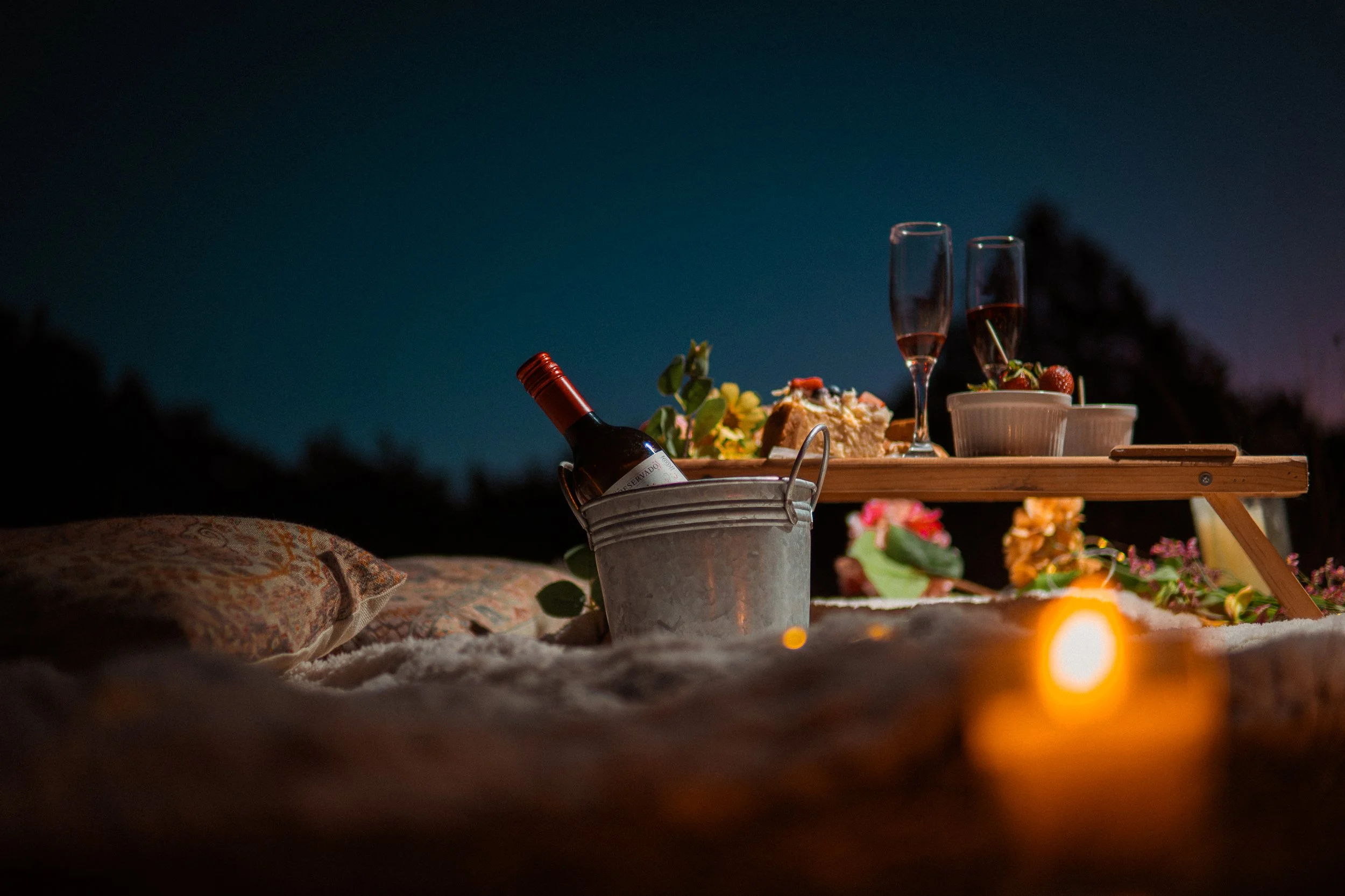 Una picnic romántica en la playa por la noche con vino, flores, frutas y velas.