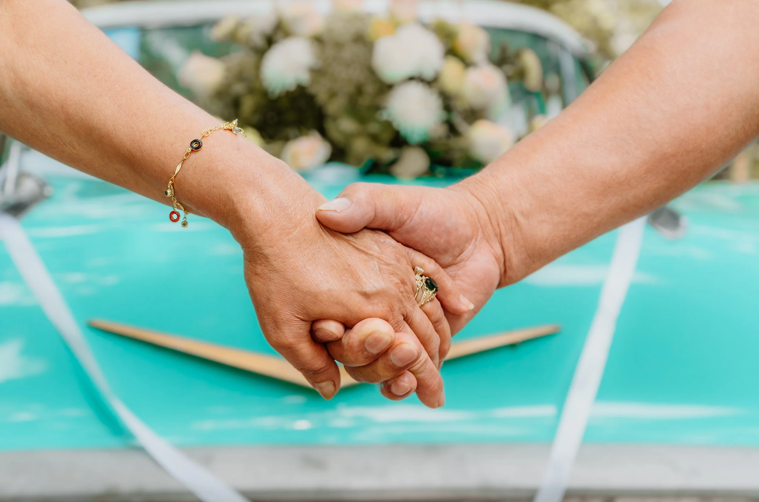 Mano y mujer entrelazadas en una boda, con fondo de flores blancas y cuna azul.