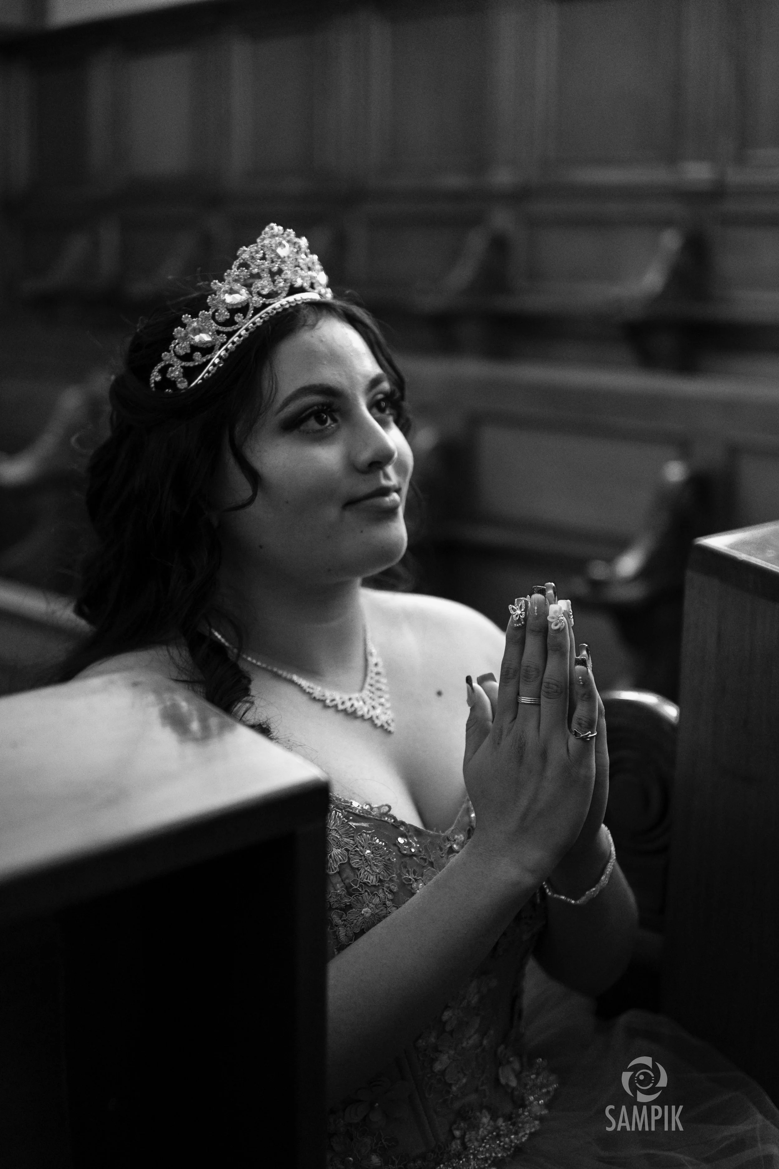 Mujer en una iglesia con tiara, rezando con las manos juntas y mostrando un vestido de boda.