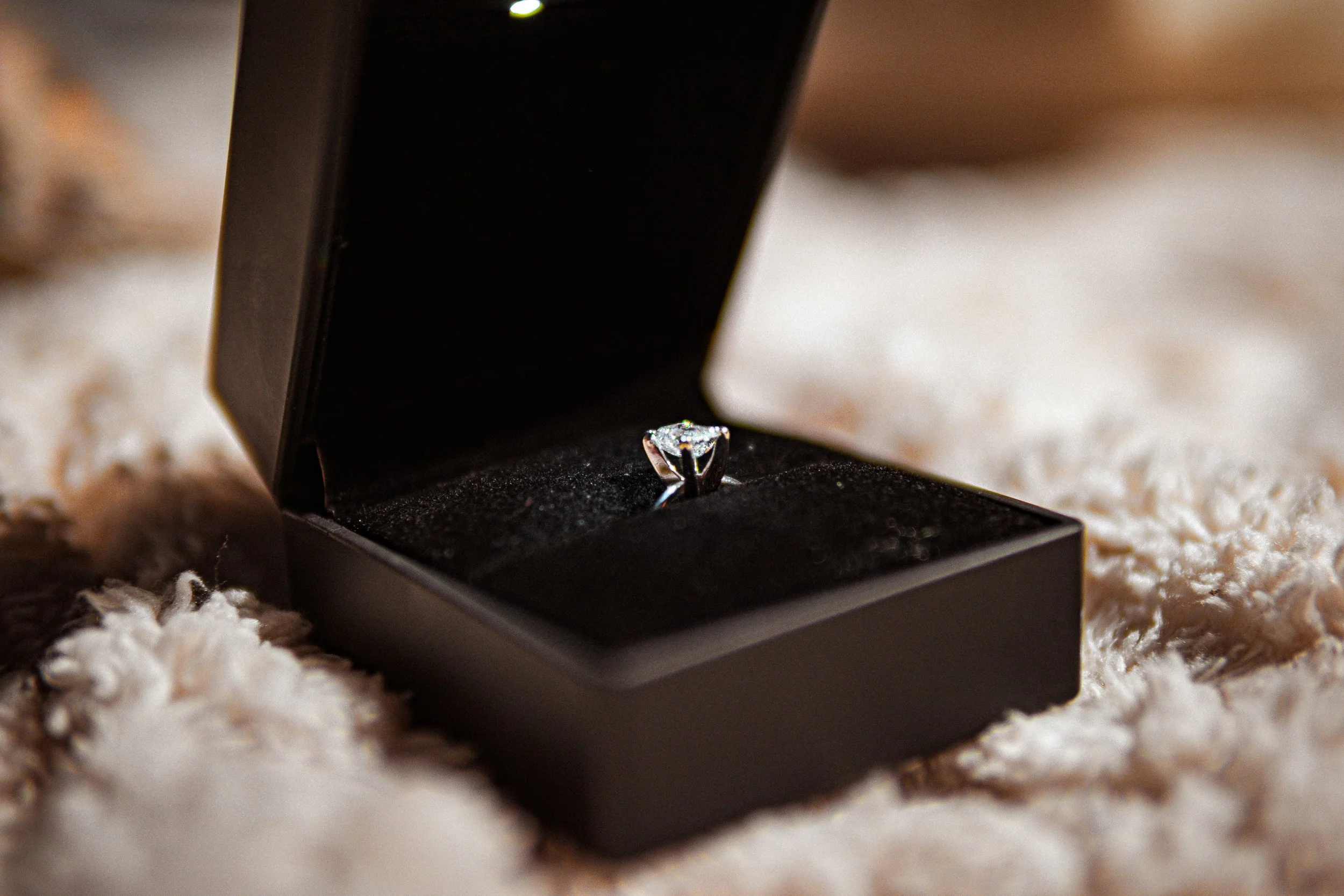 Anillo de compromiso con diamante en una caja negra sobre una superficie de peluche