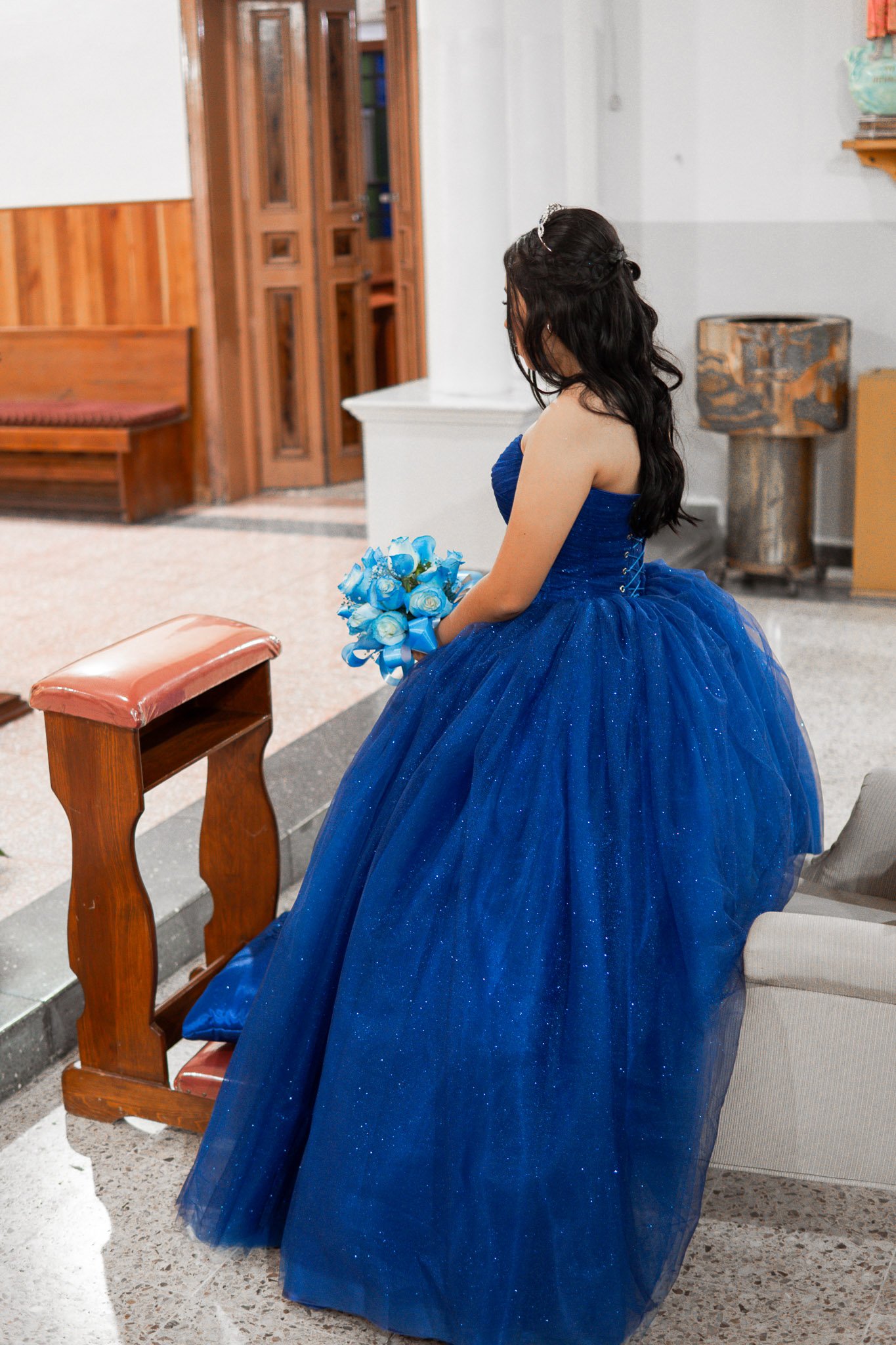 Una joven con vestido azul brillante sostiene un ramo de rosas azules en un interior.