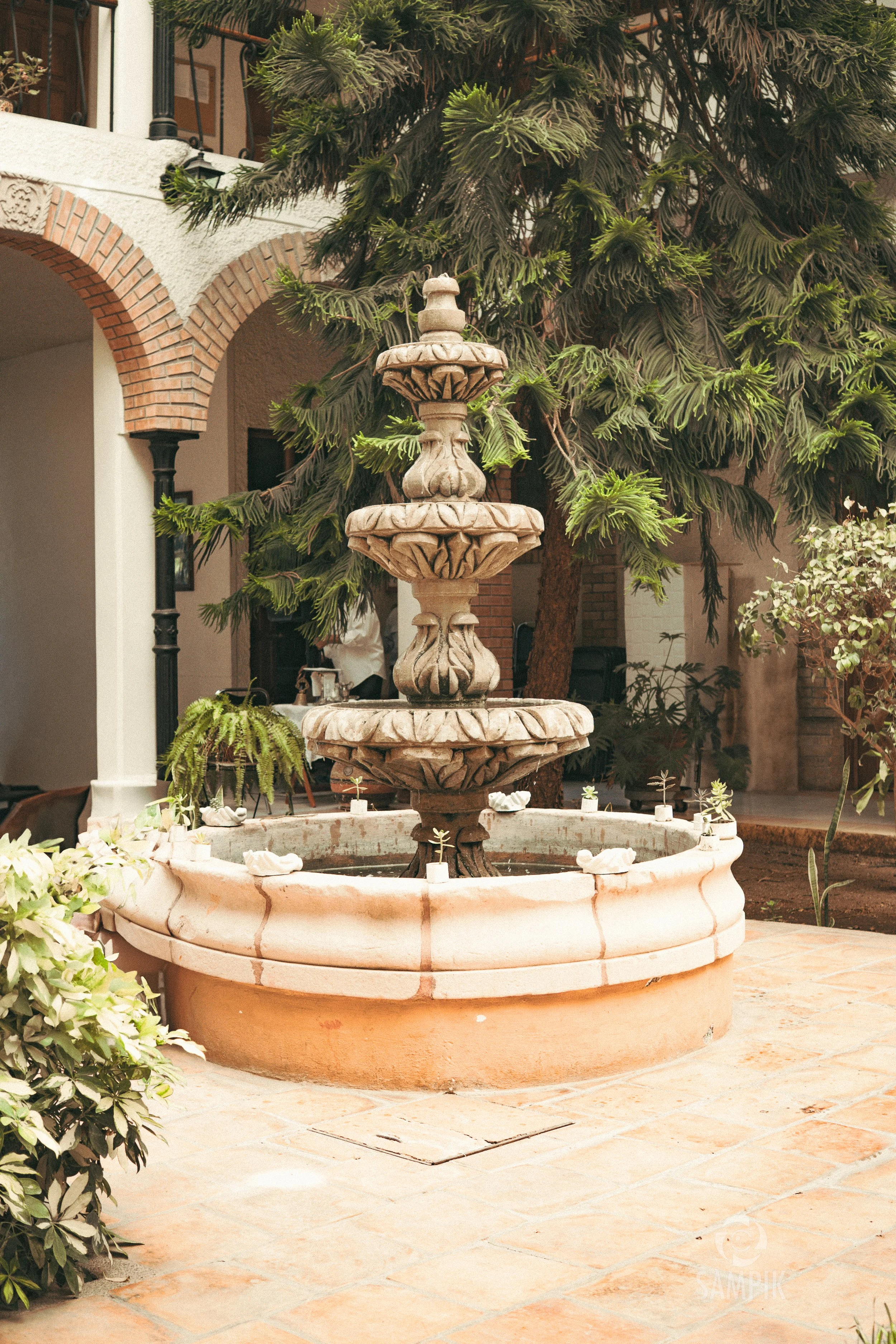 Fuente de piedra en un jardín con follaje y balcones en la parte superior.
