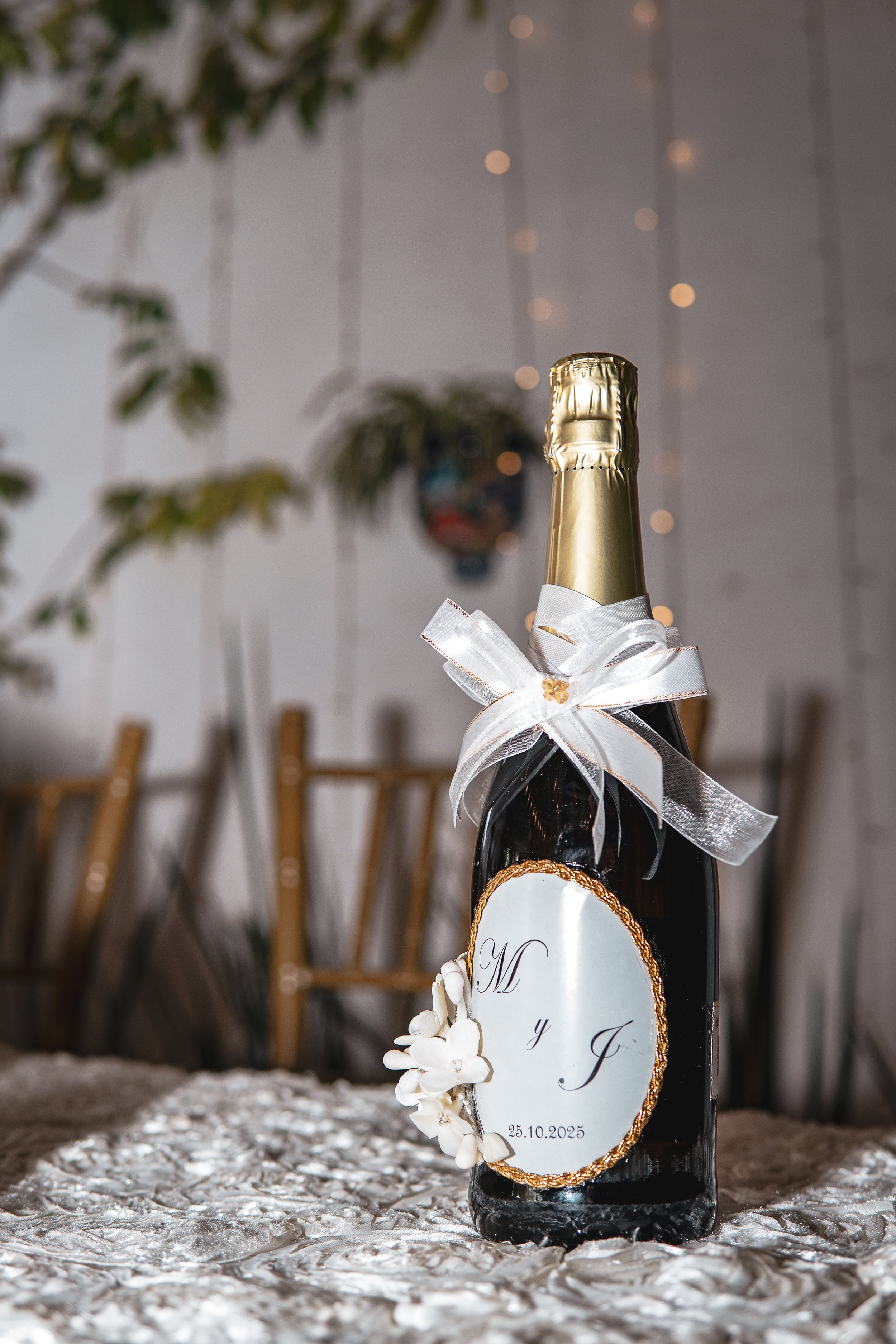 Botella de champán decorada con cinta blanca y etiqueta con iniciales y fecha, en un entorno de celebración o evento especial.