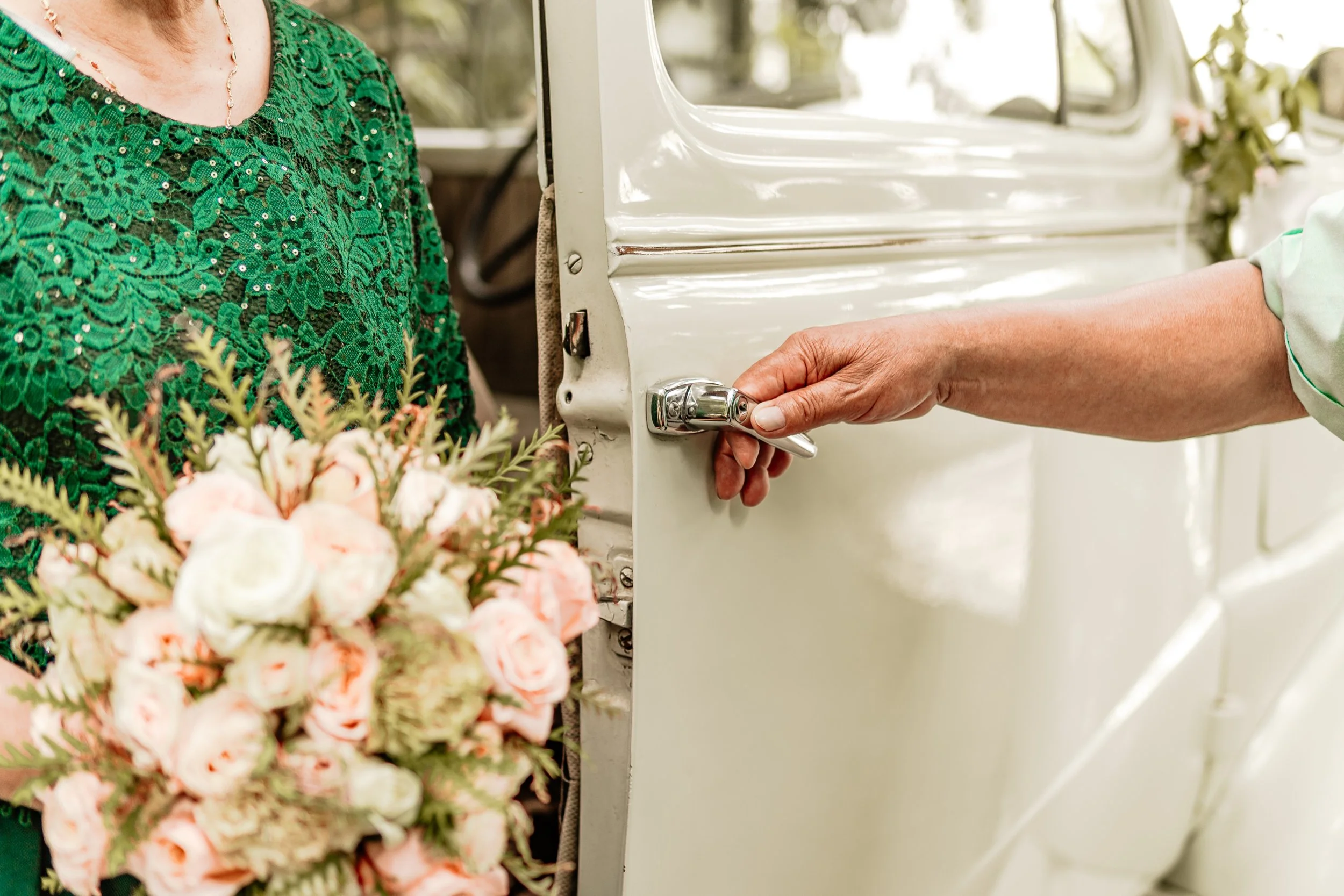 Paso en una boda en que una persona está abriendo la puerta de un automóvil vintage mientras otra le entrega un ramo de flores.