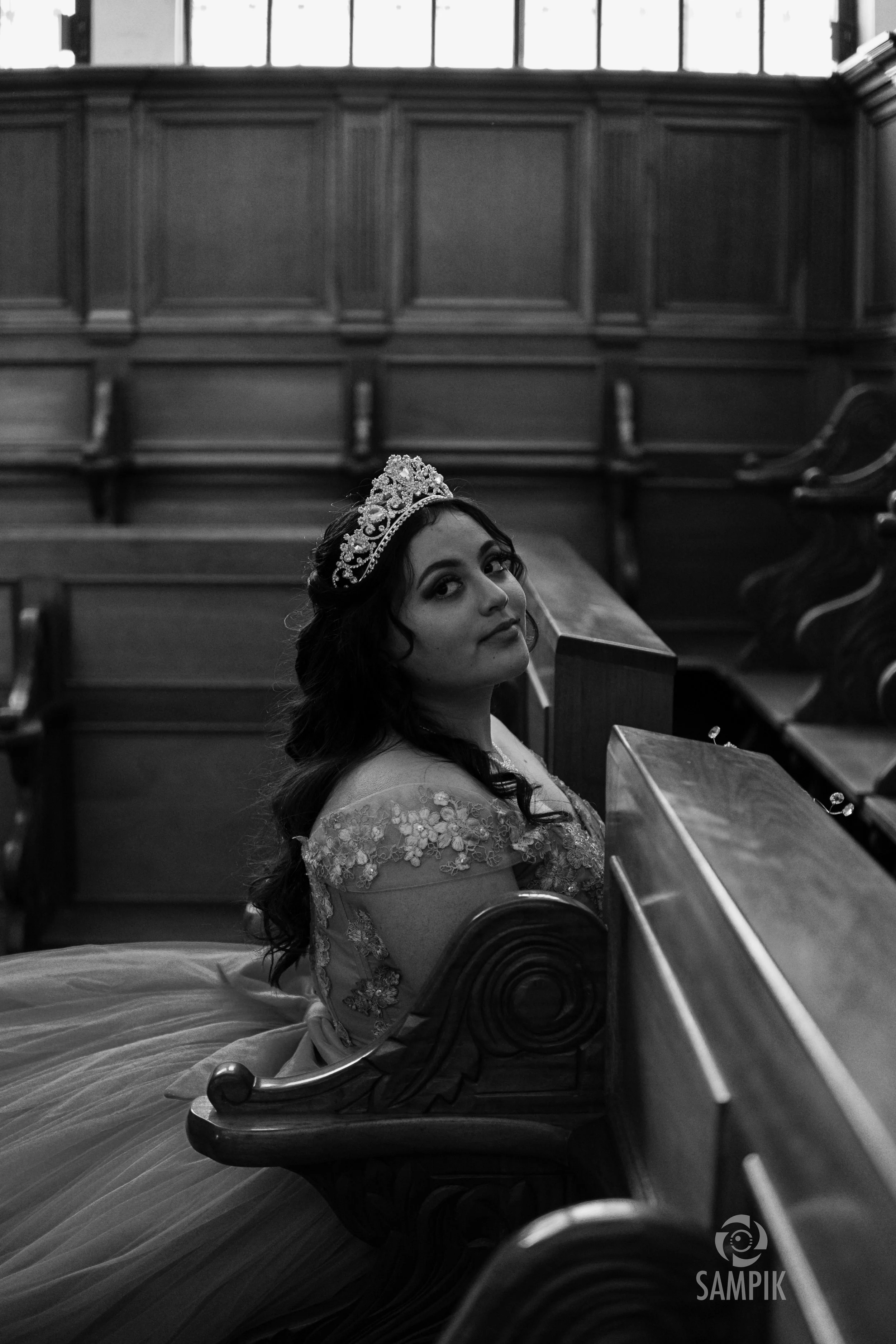 Joven mujer con corona en un salón de madera, sentada en un banco, mirando hacia la cámara.