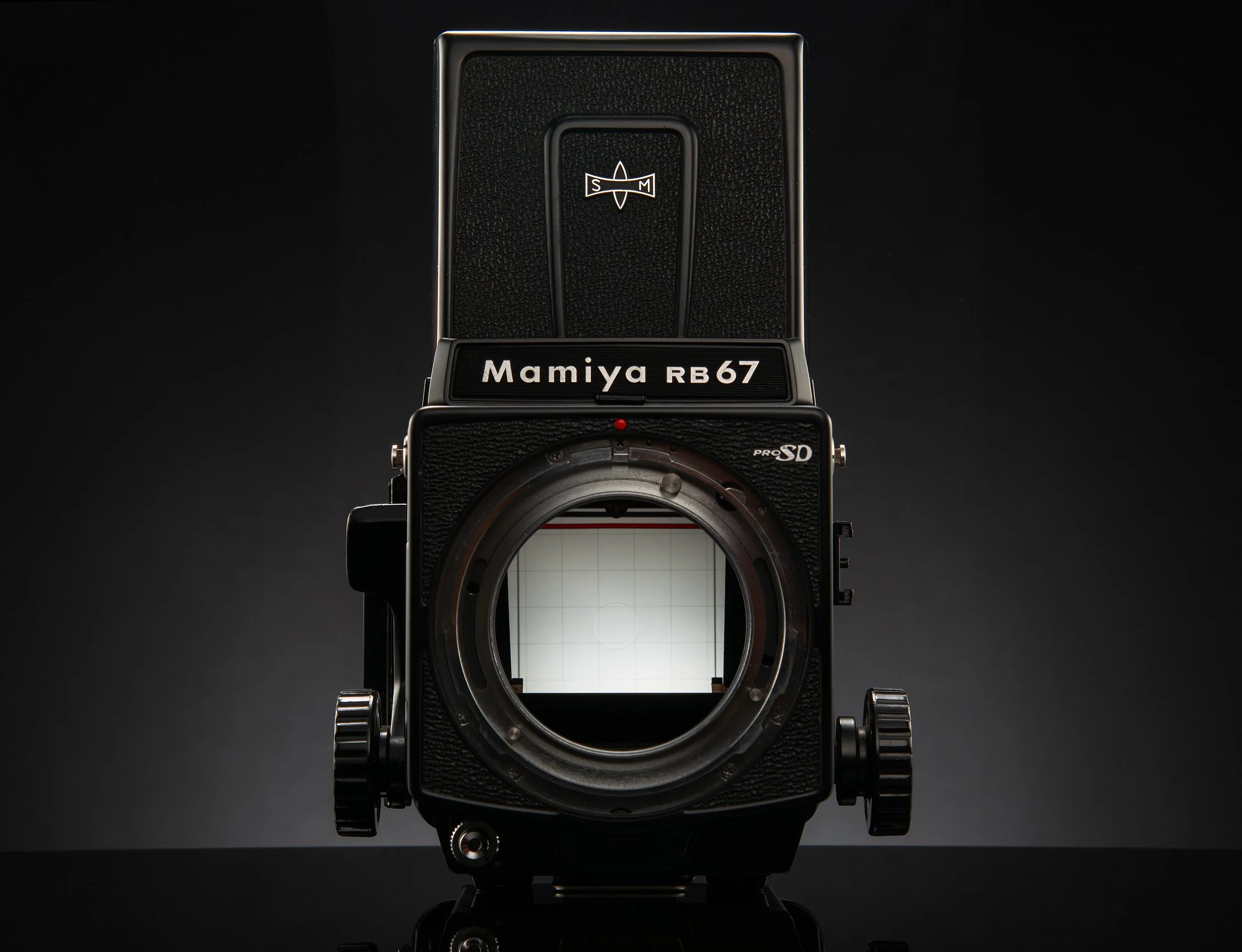 A vintage Mamiya RB67 medium format film camera with the lens removed, showing the mirror and film back exposed.
