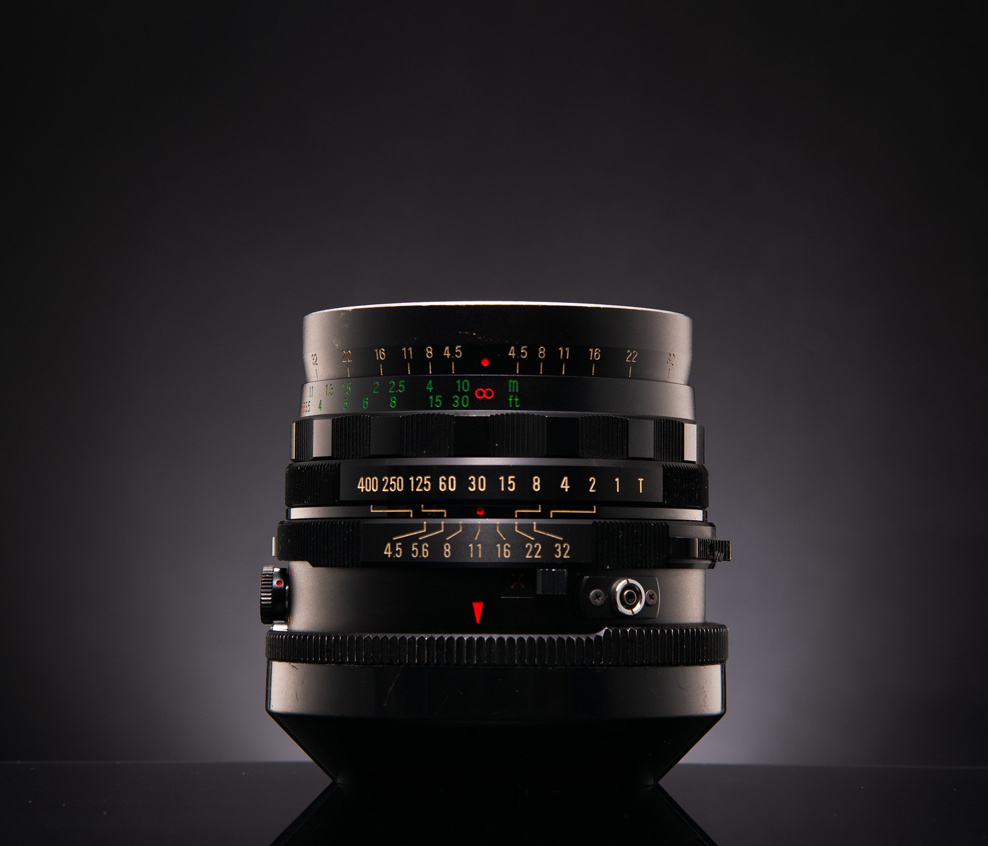 A close-up of a vintage camera lens with various focus and aperture markings against a dark background.