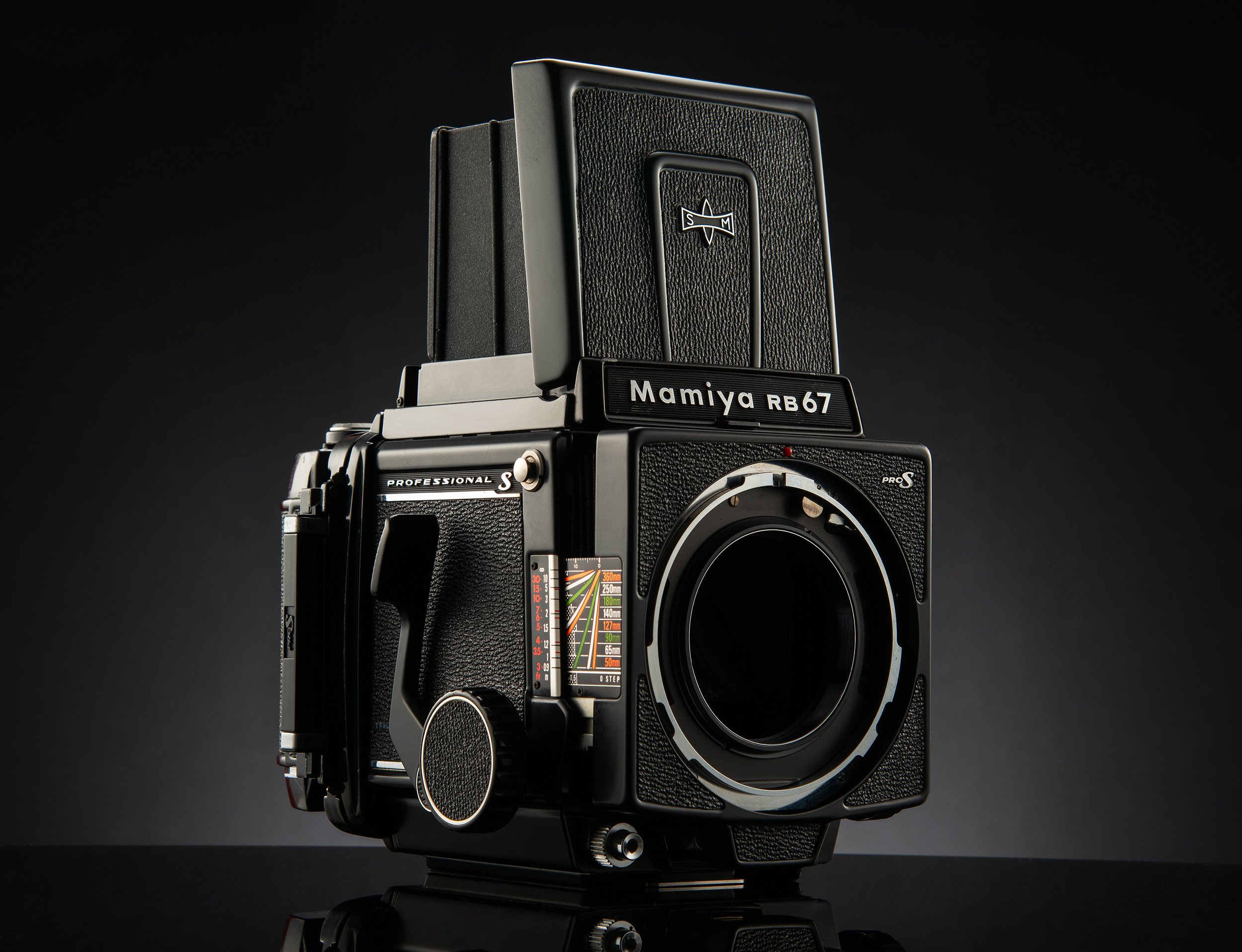 A vintage Mamiya RB67 medium format camera with a bellows focusing system and a waist-level viewfinder in a dark studio setting.