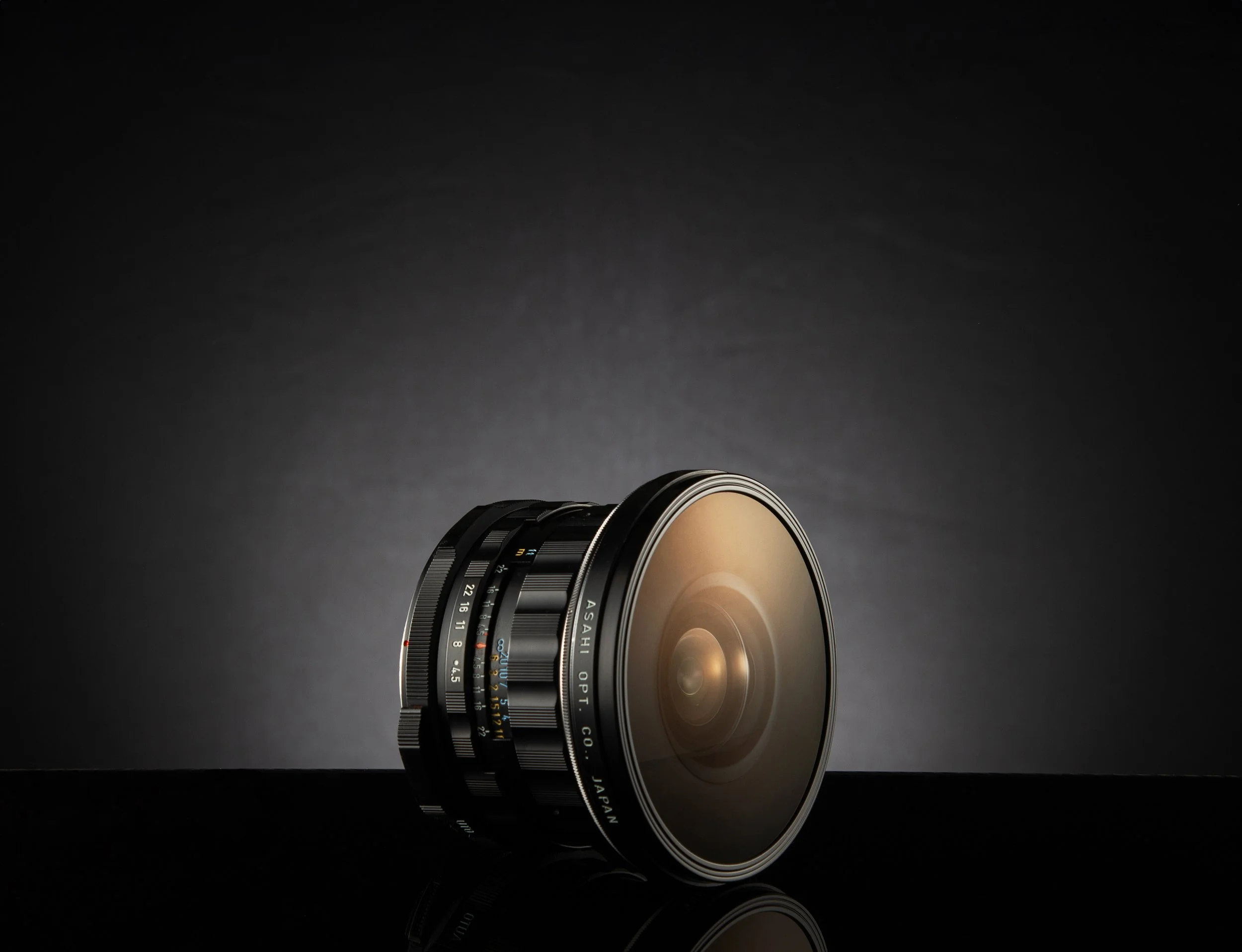 Close-up of a camera lens on a black surface against a dark background.