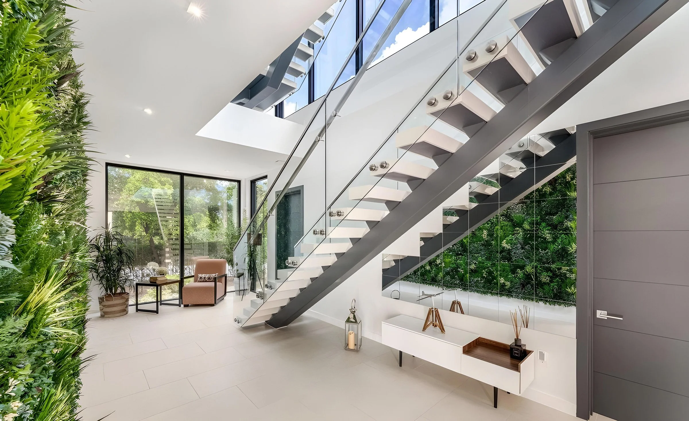 Cayman - Alive Design - Modern interior with a staircase, large window, plants, and minimalist furniture.