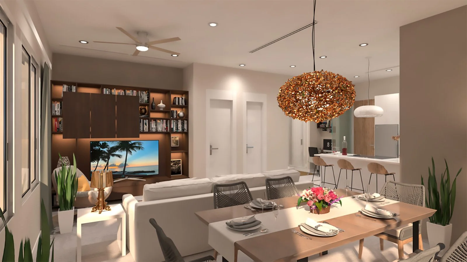Cayman - Alive Design - Interior view of a modern living and dining area with a white sofa, a glass dining table with flowers, a bookshelf with a television, and pendant lights over the kitchen area.