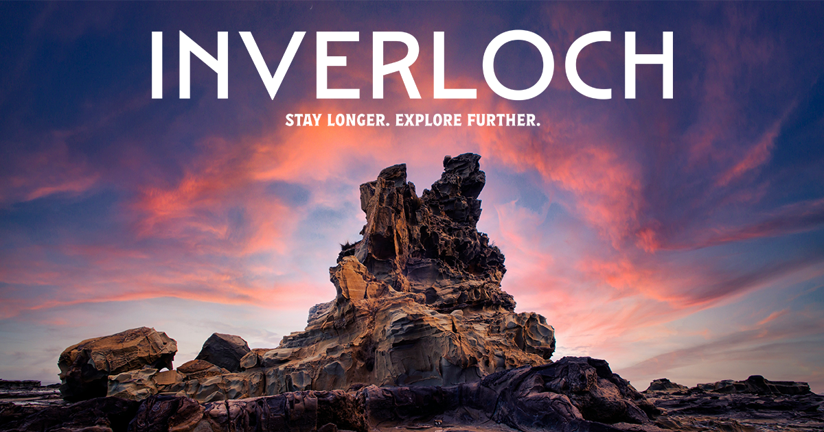 A large rock formation on a beach at sunset with pink and blue clouds in the sky, with the text 'Inverloch' and 'Stay Longer. Explore Further.'