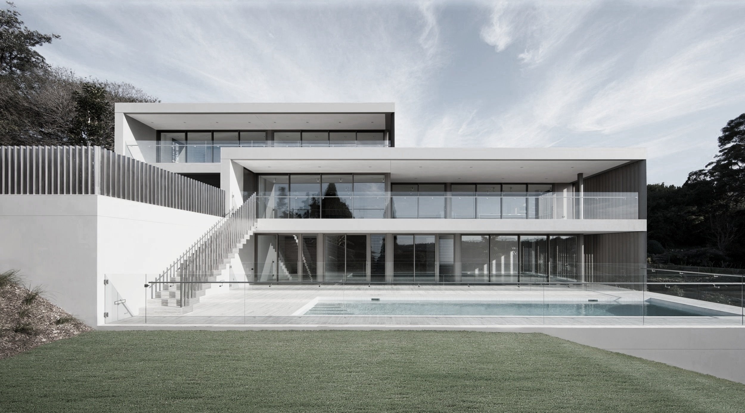 Modern multi-story house with large glass windows, balconies, and a swimming pool in the backyard, surrounded by a green lawn and trees.