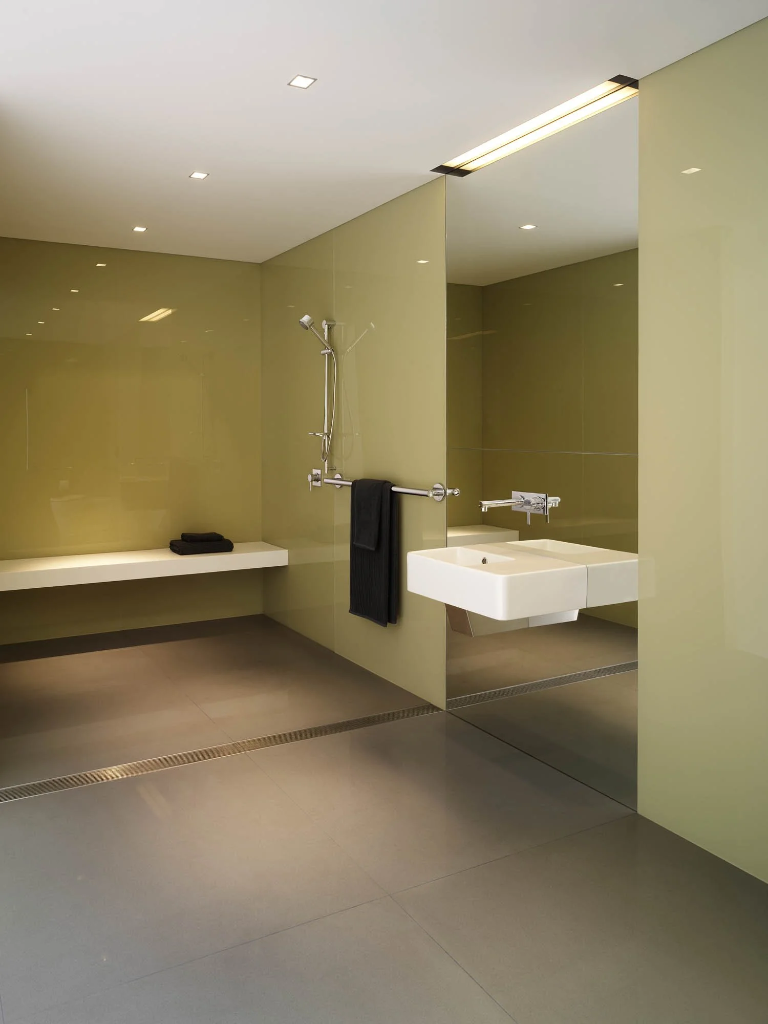 Modern minimalist bathroom with green walls, white sink, towel rack, black towel, large mirror, and ceiling lights.