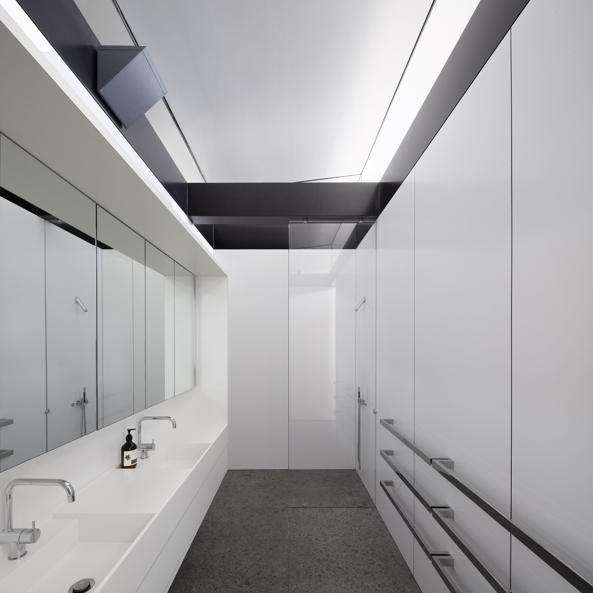 Minimalist white bathroom interior with dual sinks, mirror, black soap dispenser, and gray flooring.