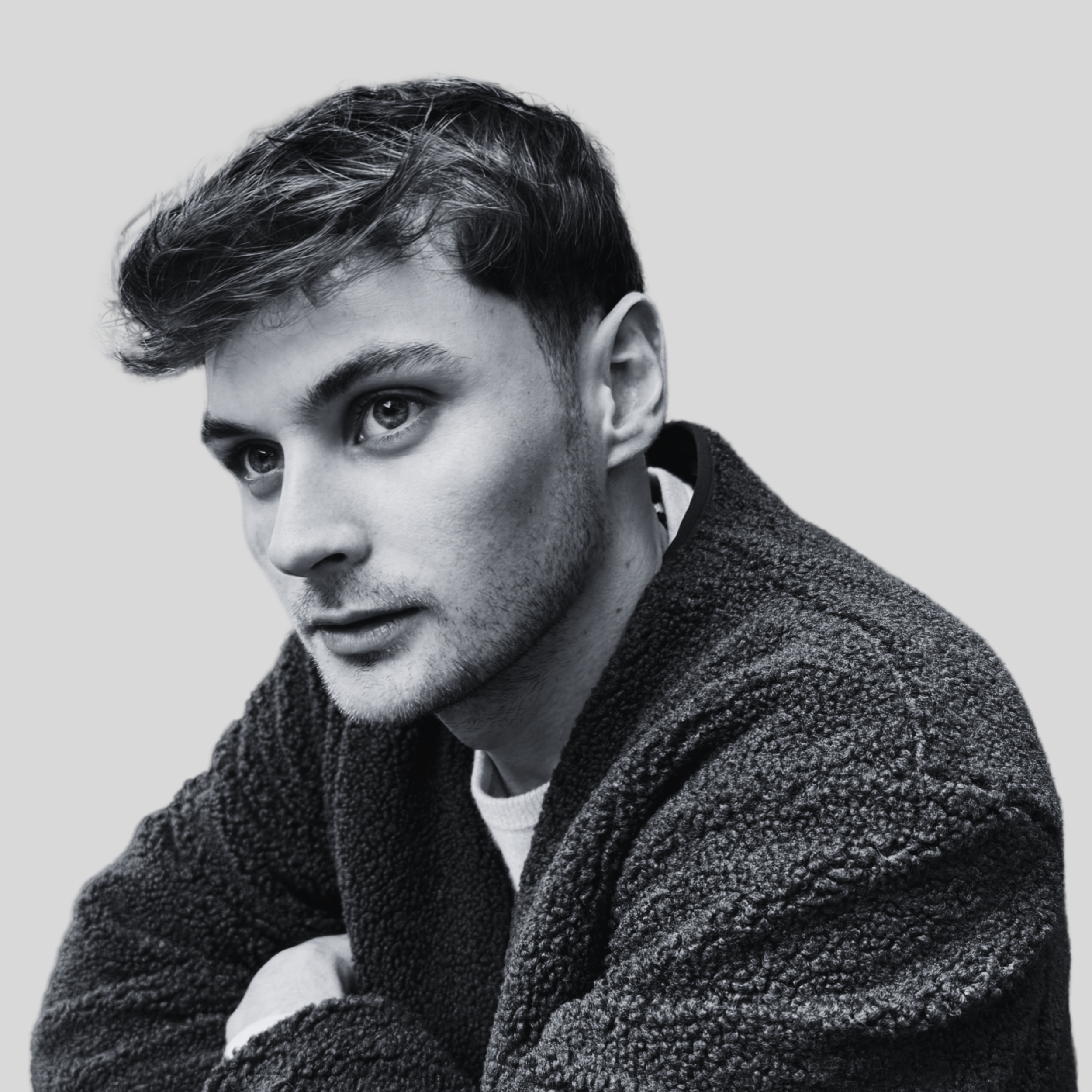 Black and white portrait of a young man with short hair, wearing a textured jacket, gazing thoughtfully to the side.