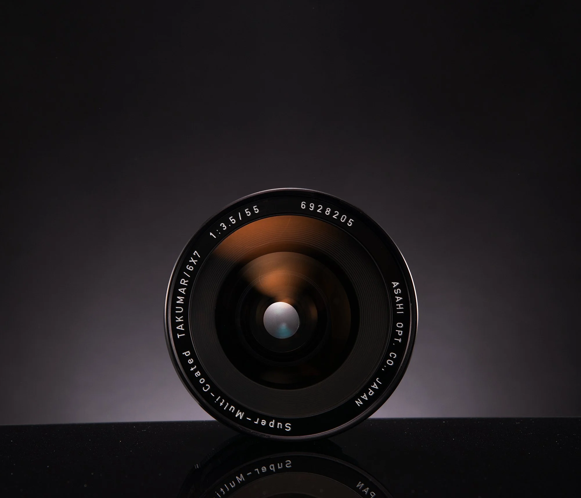 Close-up of a camera lens with black background and reflection on surface.