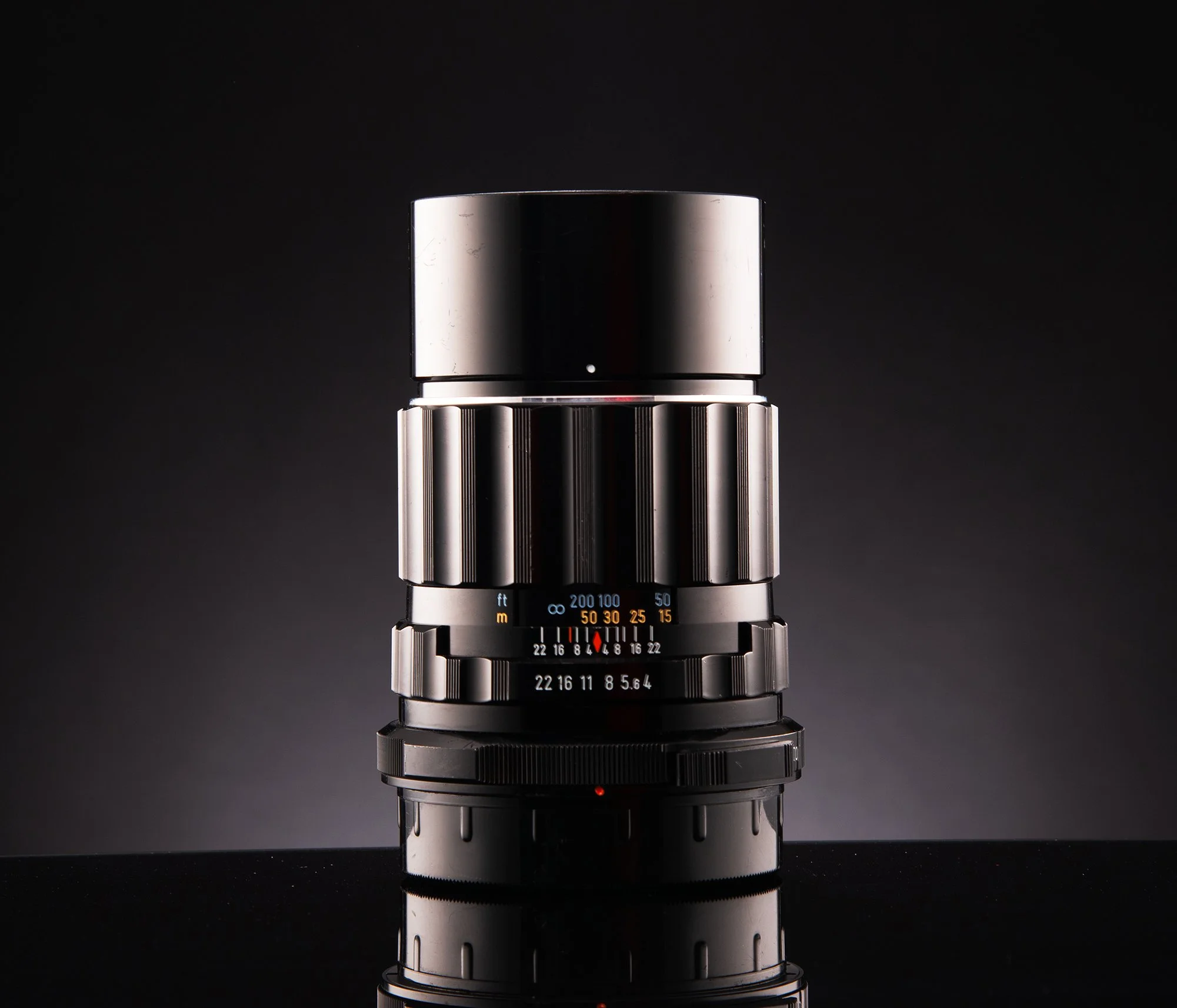 A vintage camera lens with a black background and reflection on the surface beneath it.