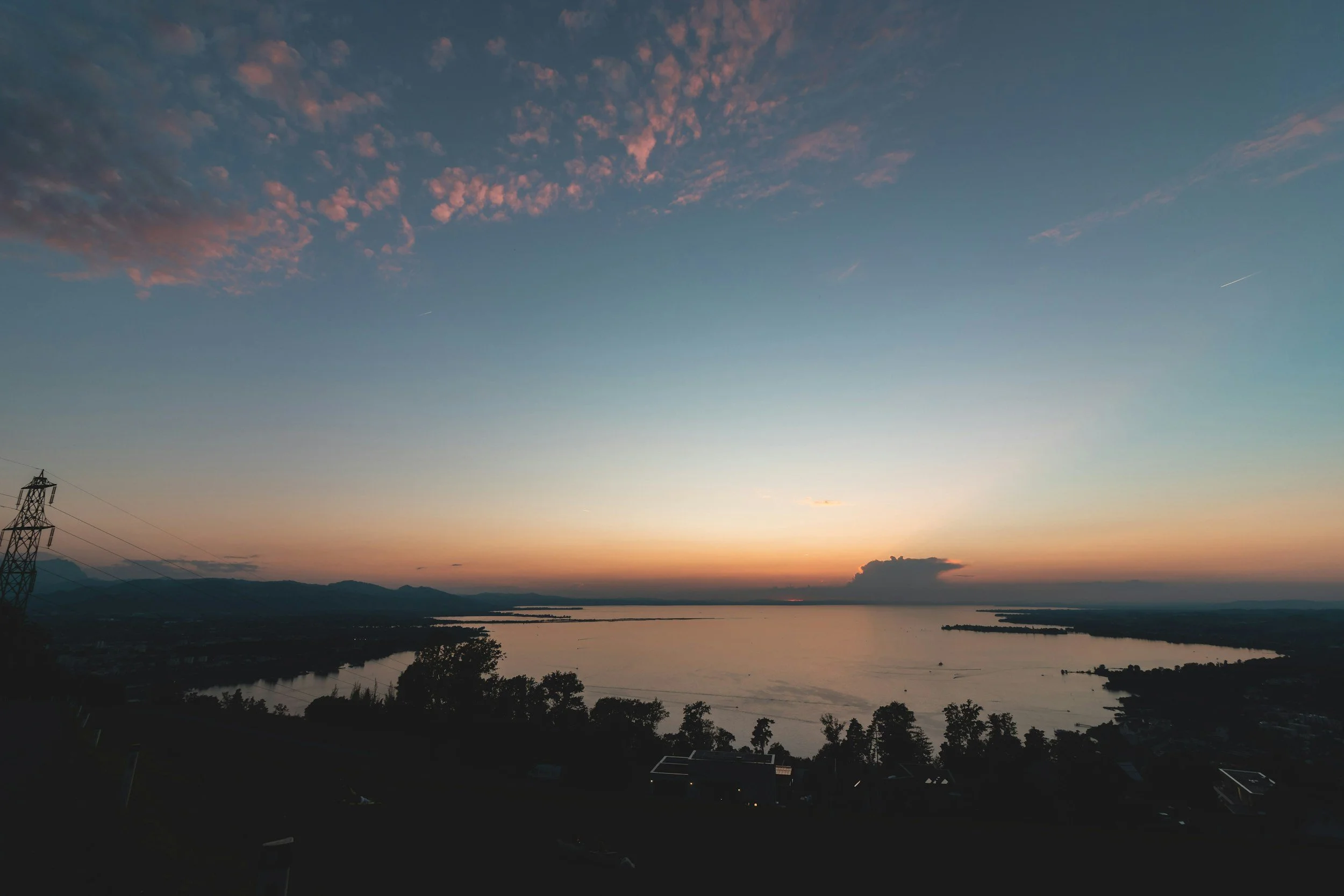 A sunset over a river with silhouettes of trees and mountains in the distance.