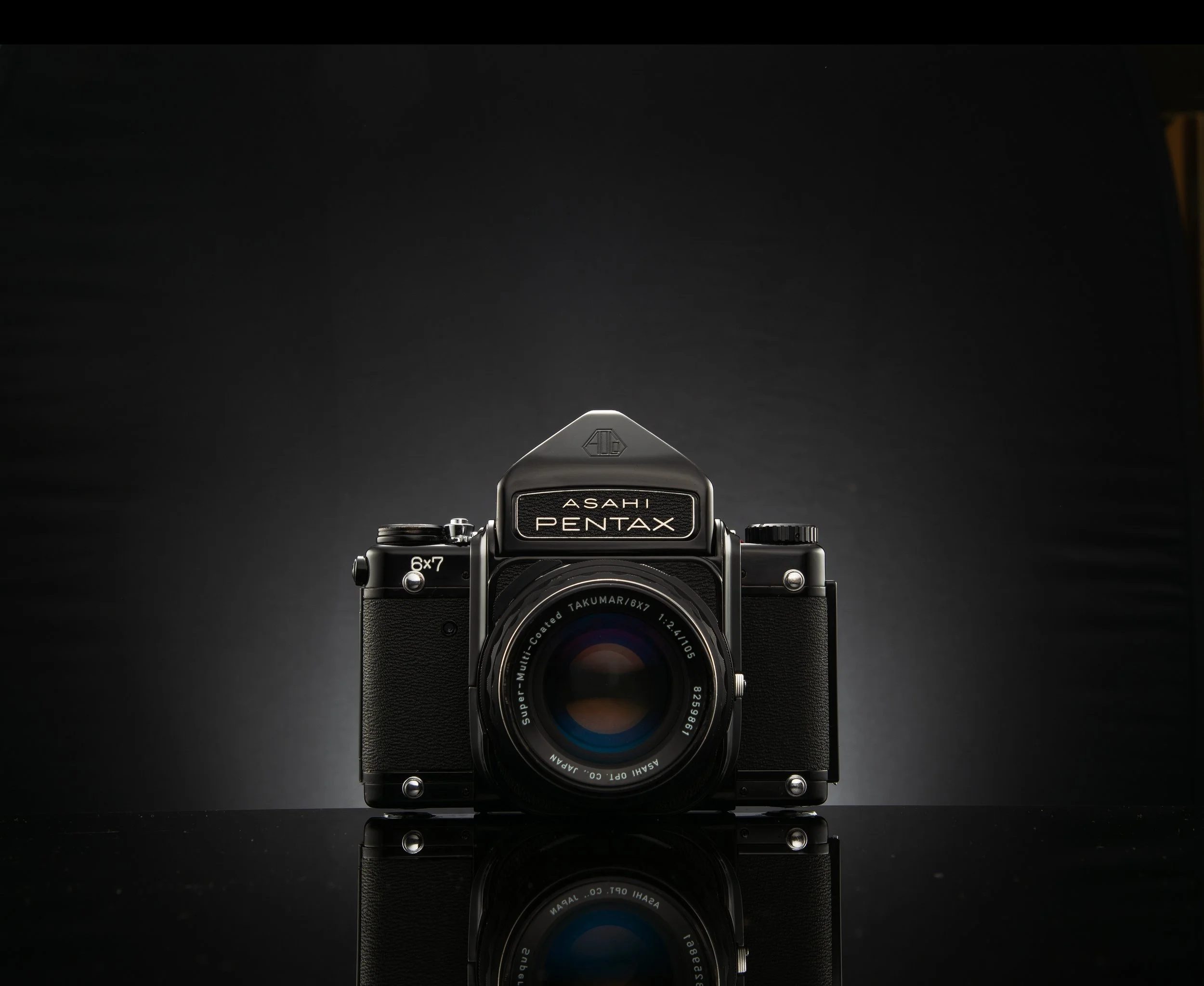 A vintage camera labeled 'Asahi Pentax' with a Takumar lens, placed on a reflective black surface against a dark background.