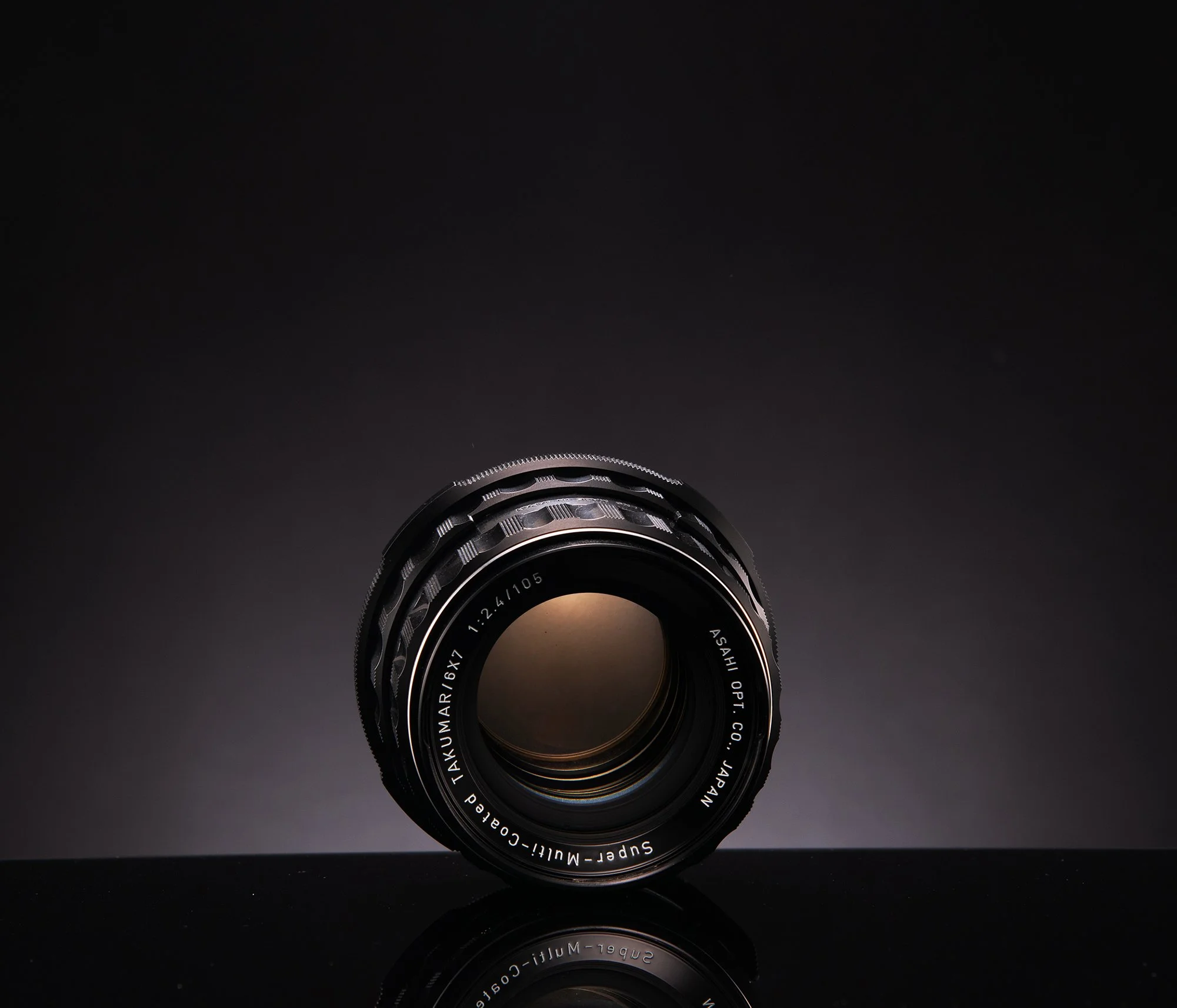 Close-up of a camera lens against a black background with reflective surface.