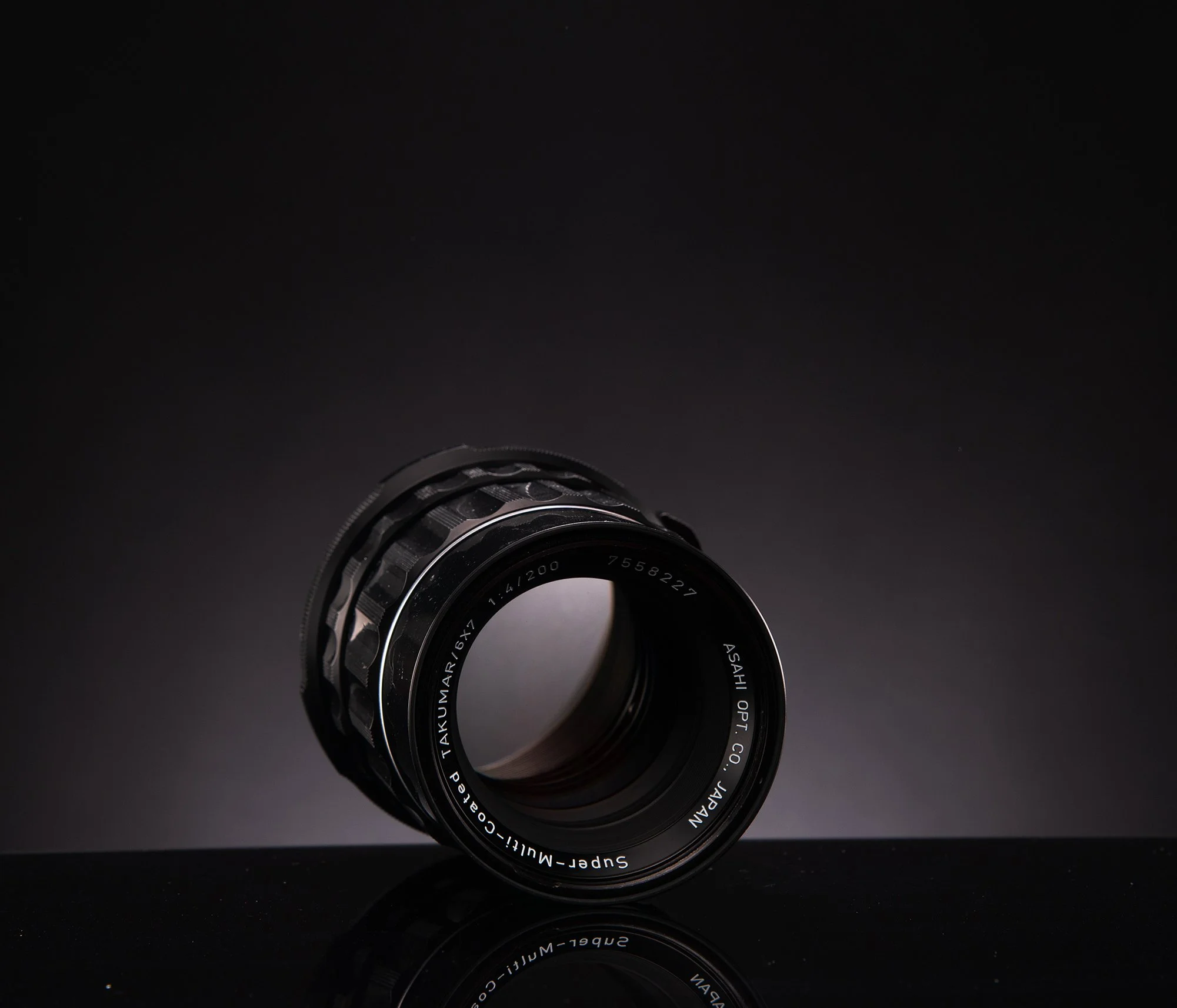 Close-up of a camera lens against a dark background with a reflective surface.