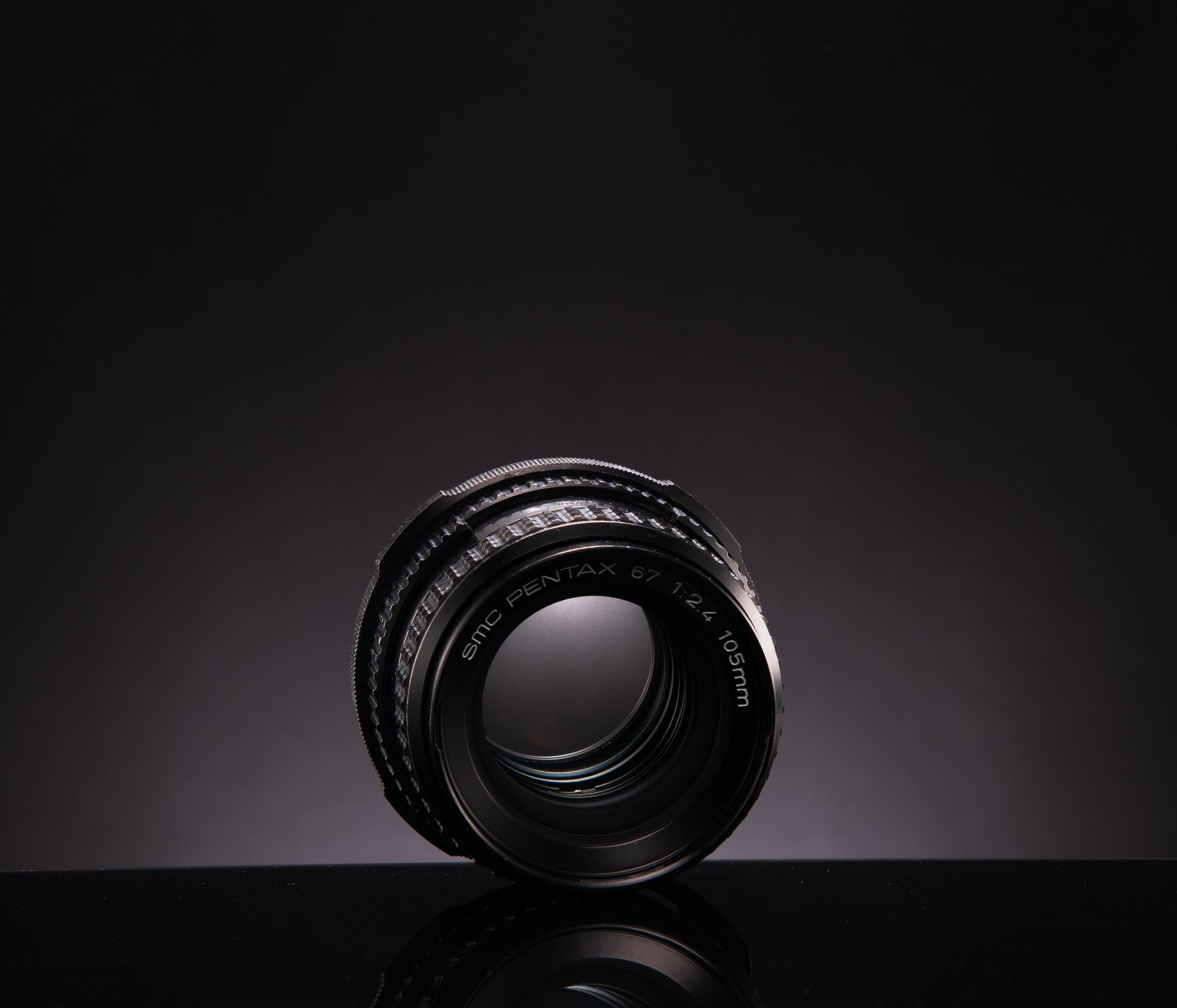 Camera lens placed on a reflective surface with a dark gradient background.