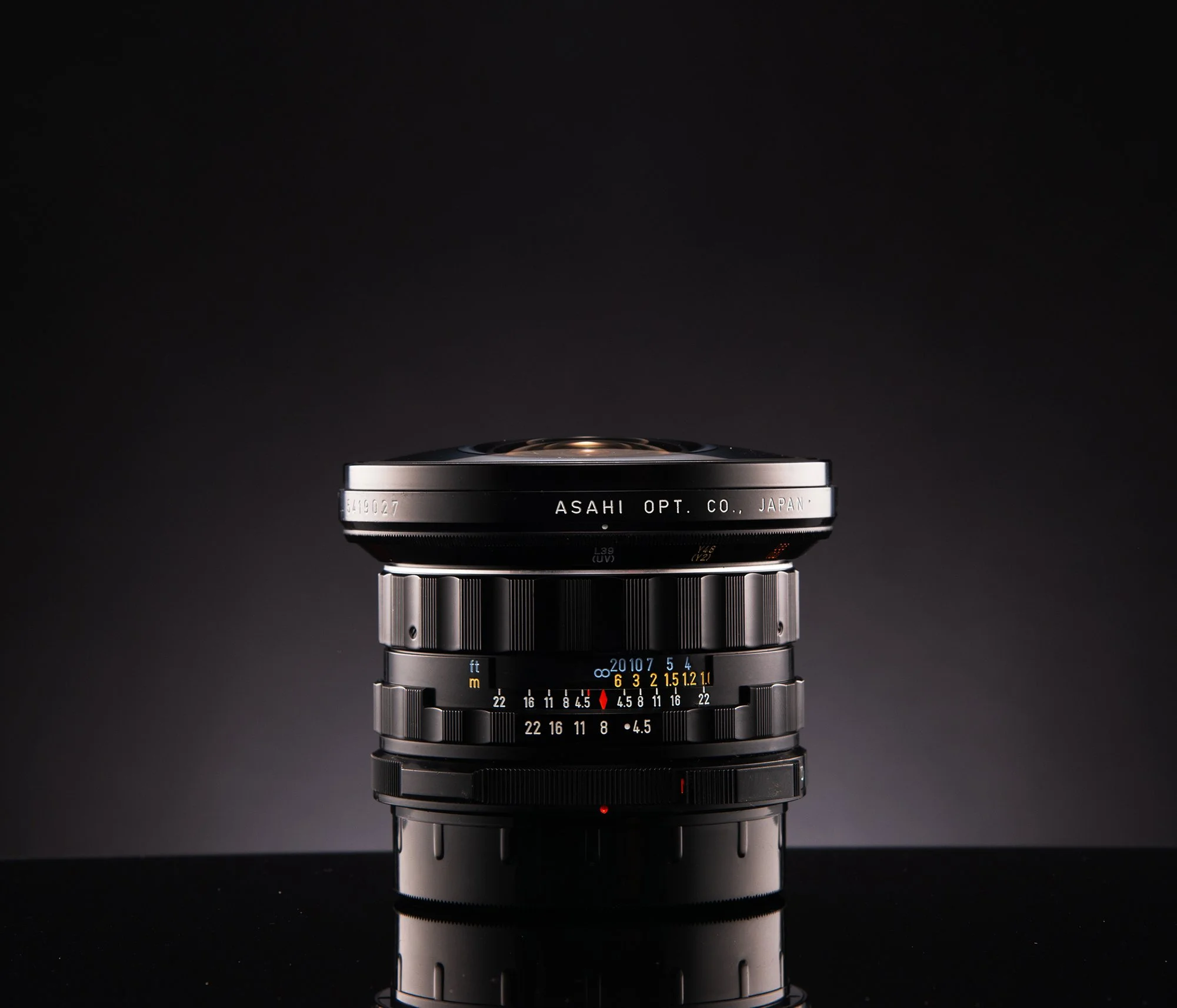 A vintage camera lens with a black background, reflecting on a glossy black surface.