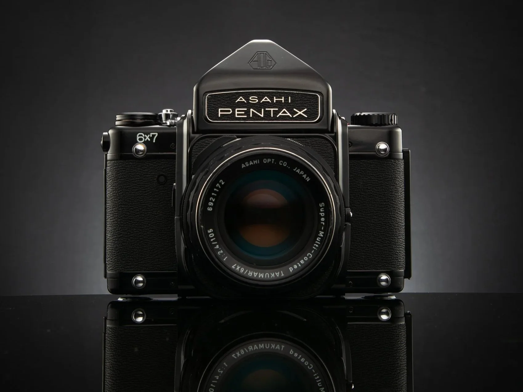 A black vintage Asahi Pentax camera with a large lens, displayed against a dark background with a reflection below.