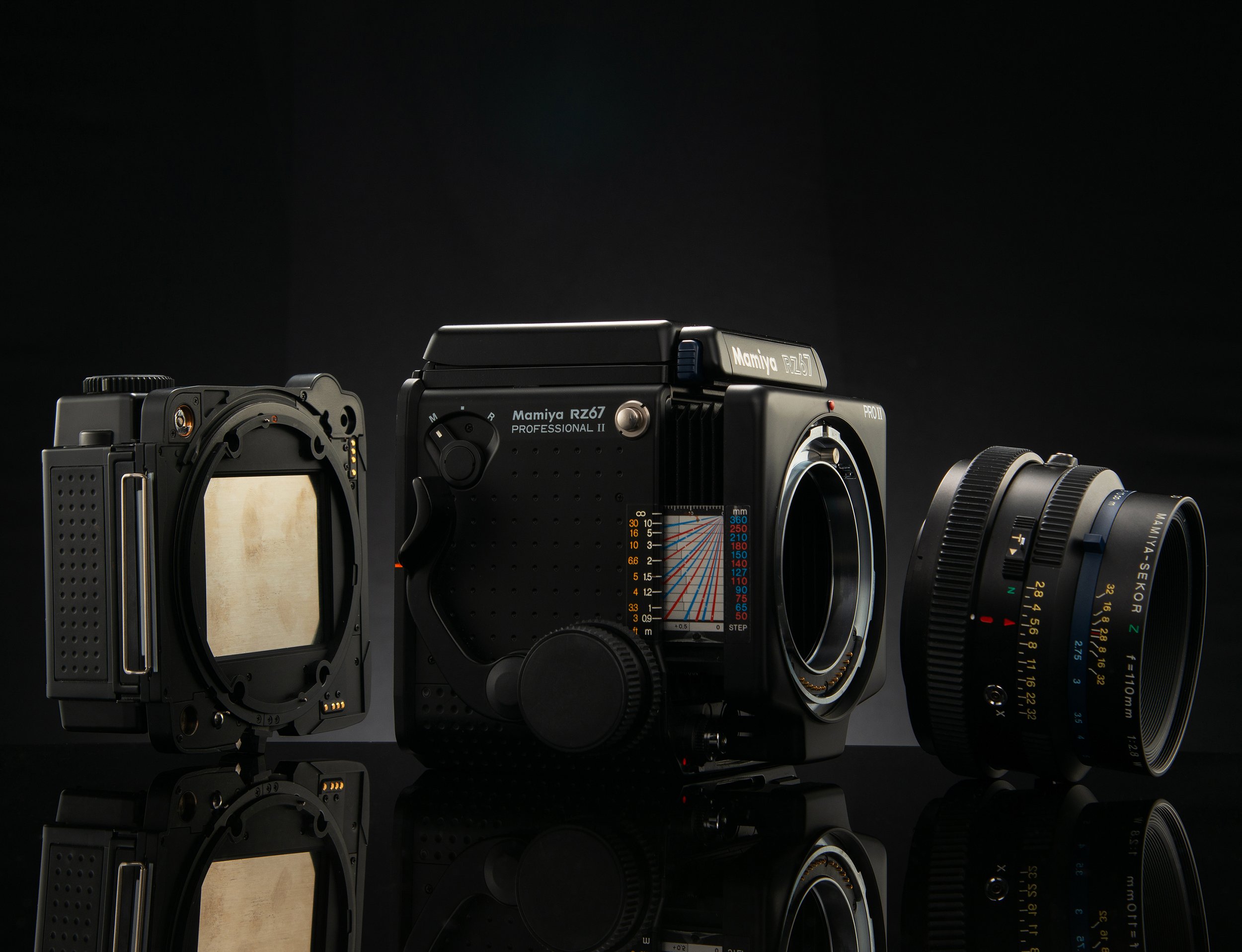 Disassembled Mamiya RZ67 camera with lens and mirror components on a reflective black surface.