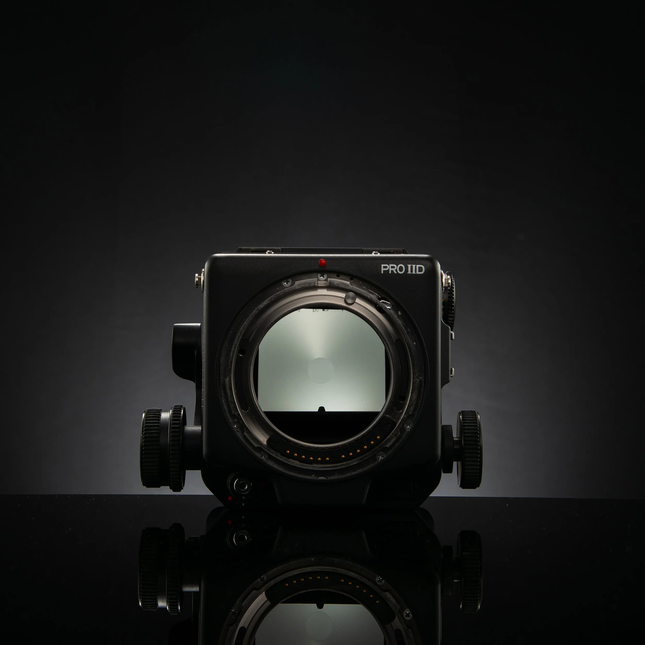 A professional camera without a lens attached, showing the sensor inside, on a glossy black surface with a dark background.