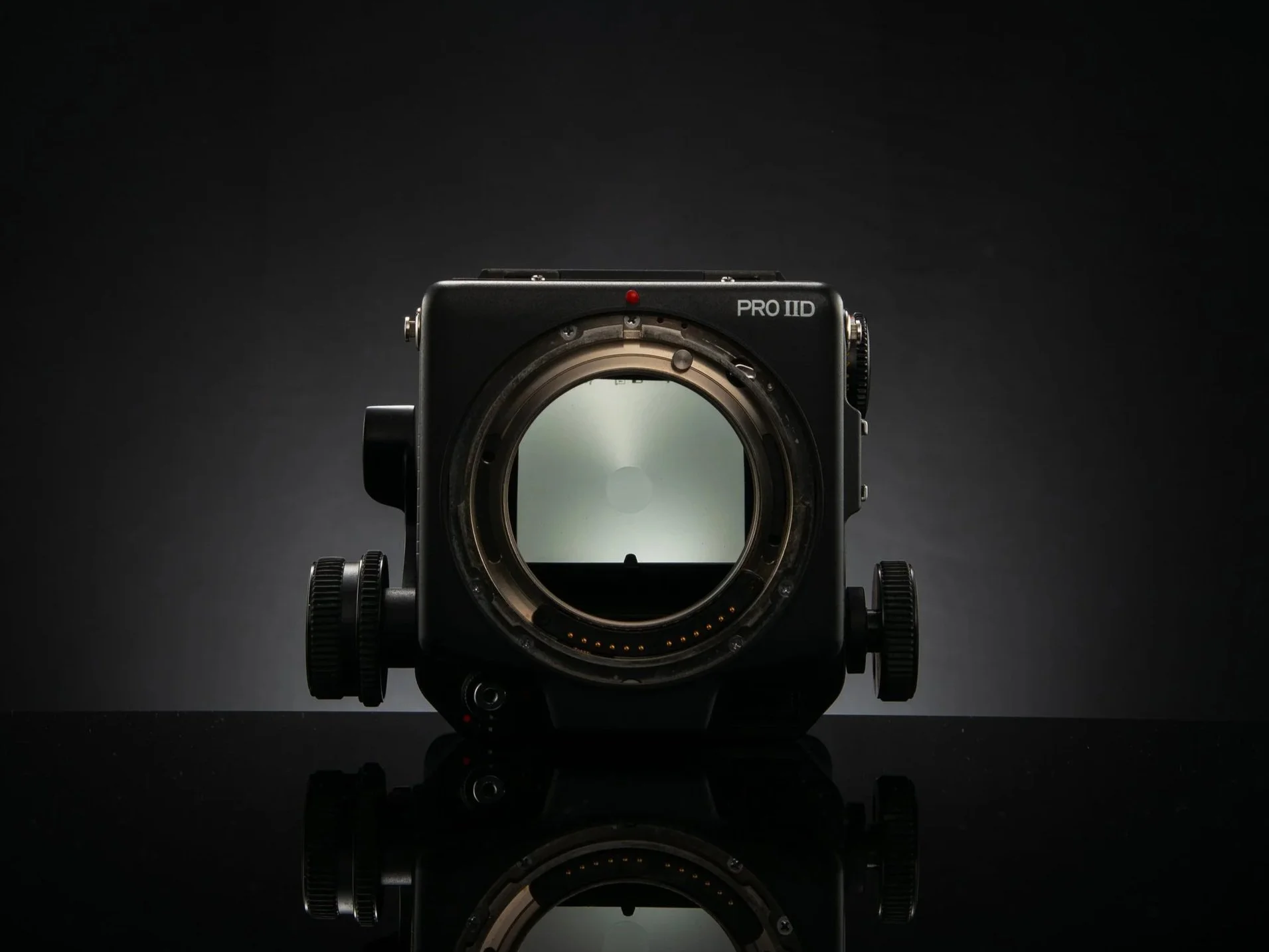 Mamiya Rz67 Pro ii body without a lens, showing the mirror inside, against a dark background with a reflective surface beneath.