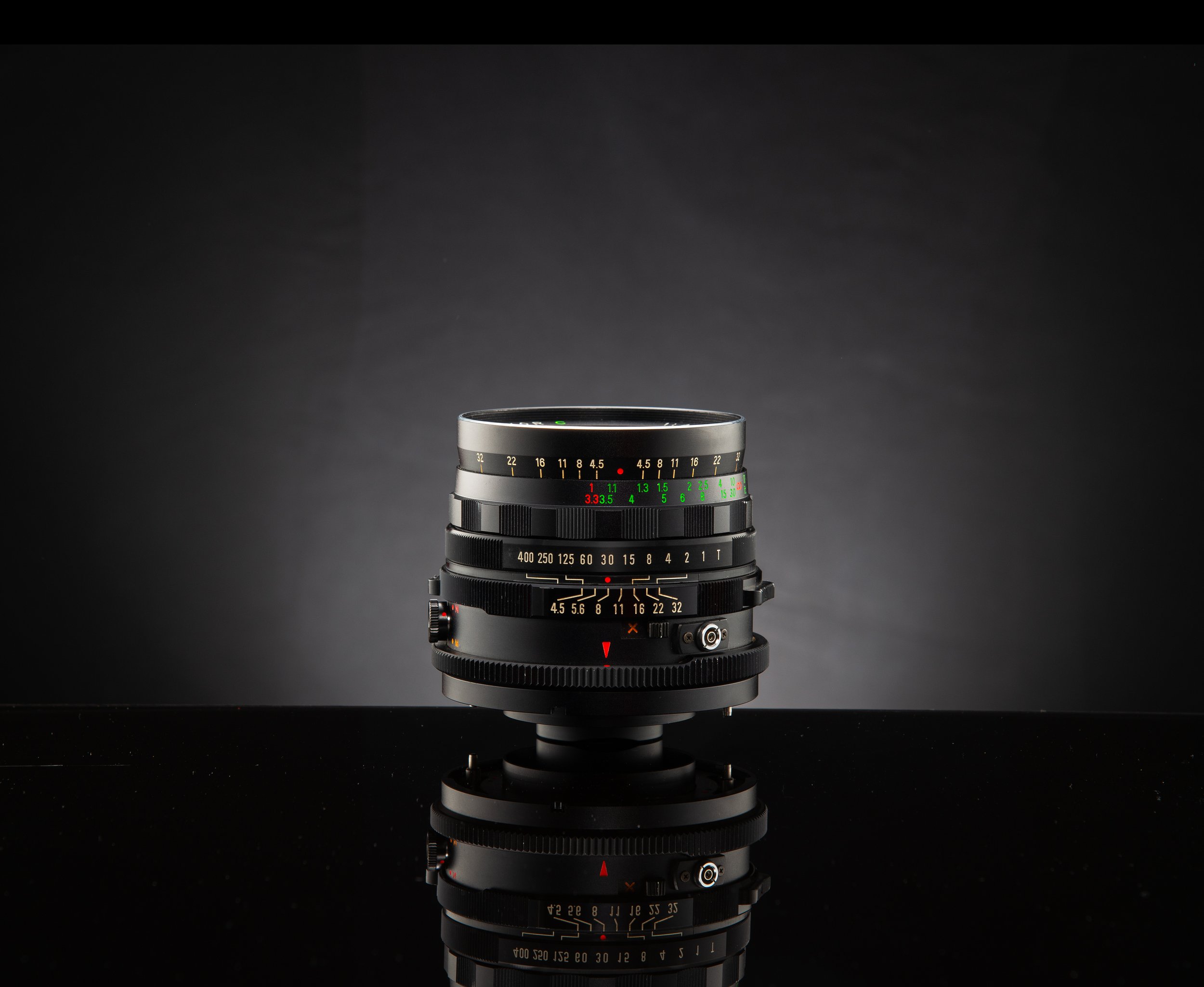 A camera lens placed on a reflective black surface against a dark background.