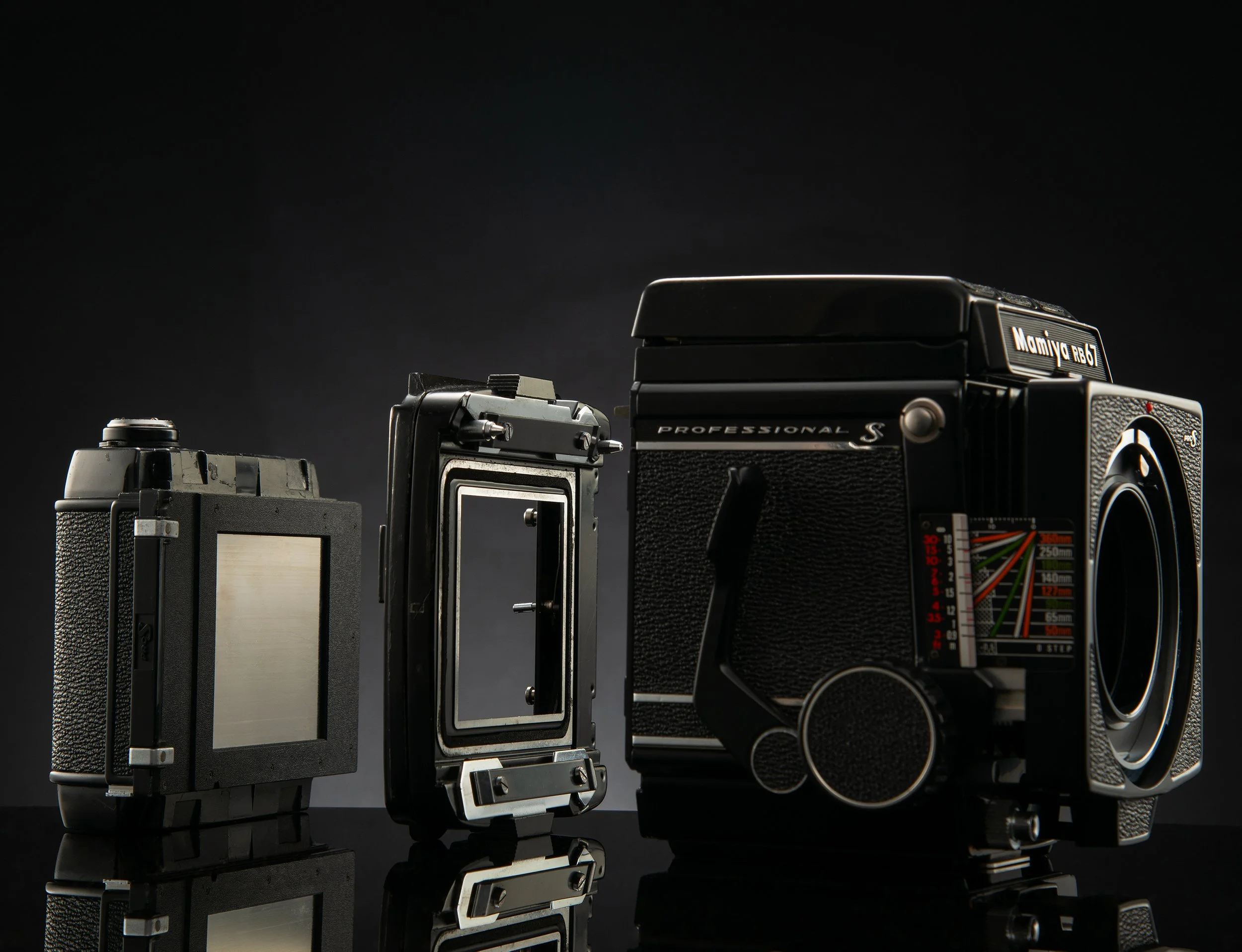 A professional film camera with two lens attachments on a black reflective surface with a dark background.