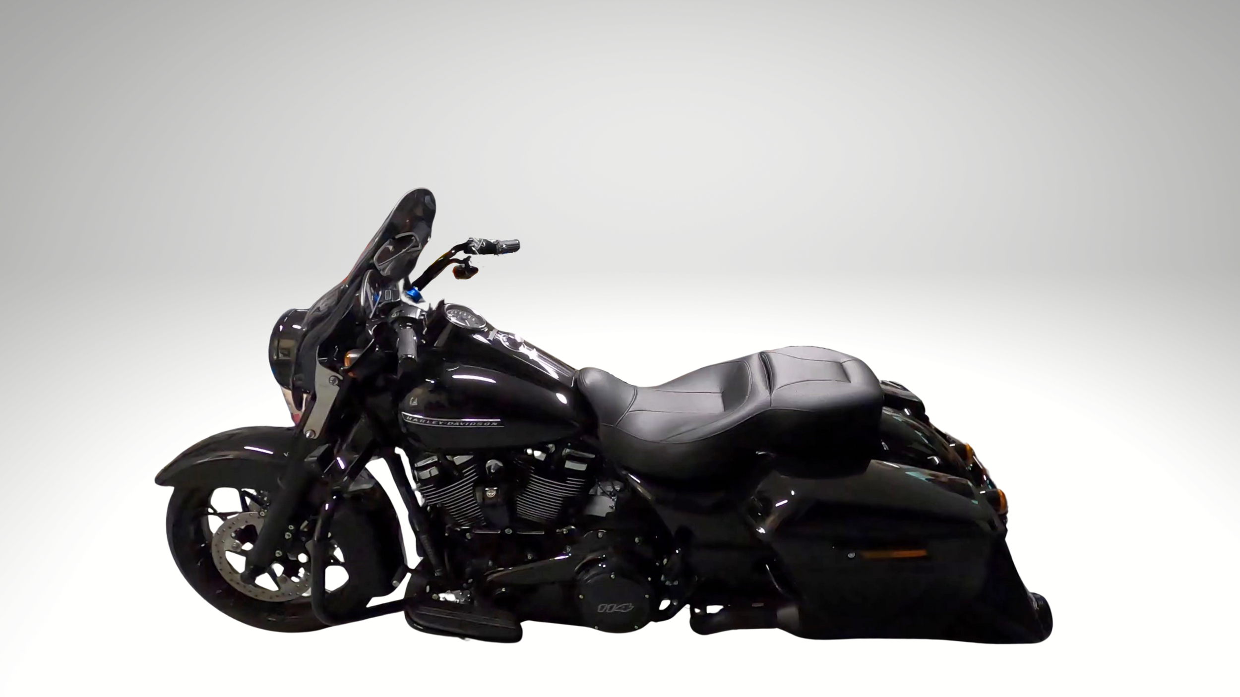 Black Harley-Davidson touring motorcycle with a windshield, black leather seat, and saddlebags, positioned against a plain gradient background.