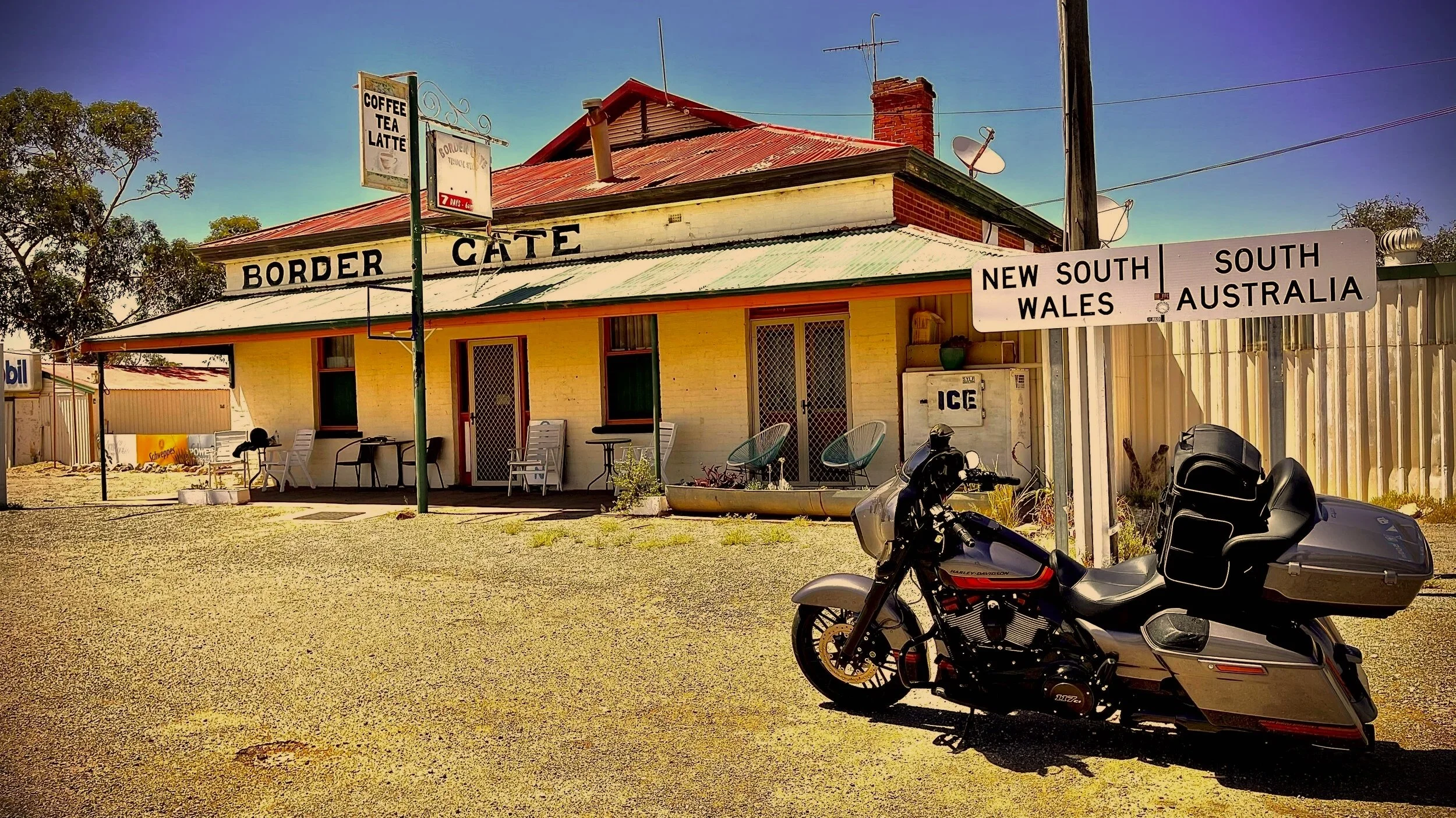 Border crossing building with signs indicating New South Wales, South Australia, and the border gate, with a motorcycle parked in front.
