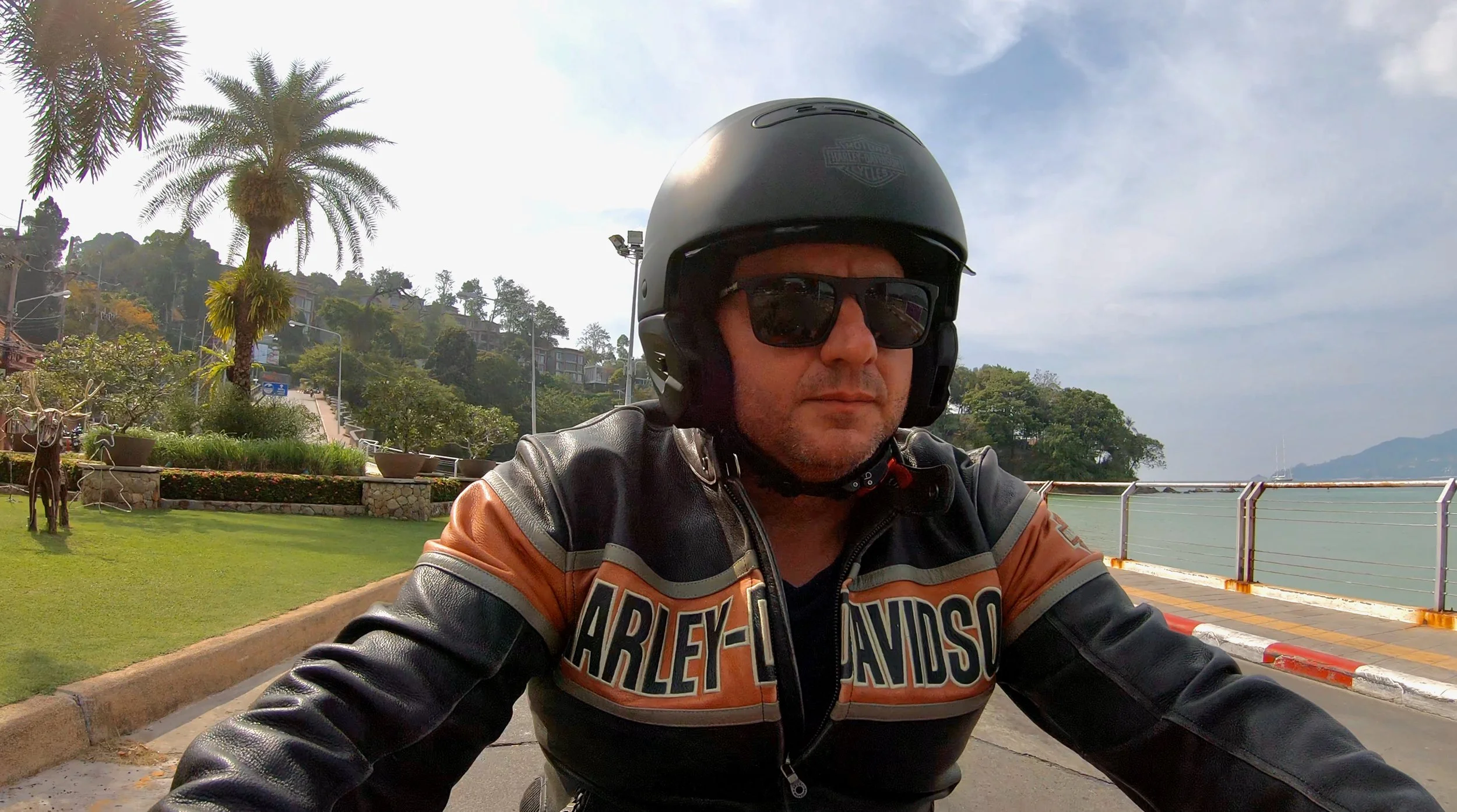 A sunset view over a body of water, with a Buddha statue in the foreground on a hill, overlooking a landscape of hills and distant islands.