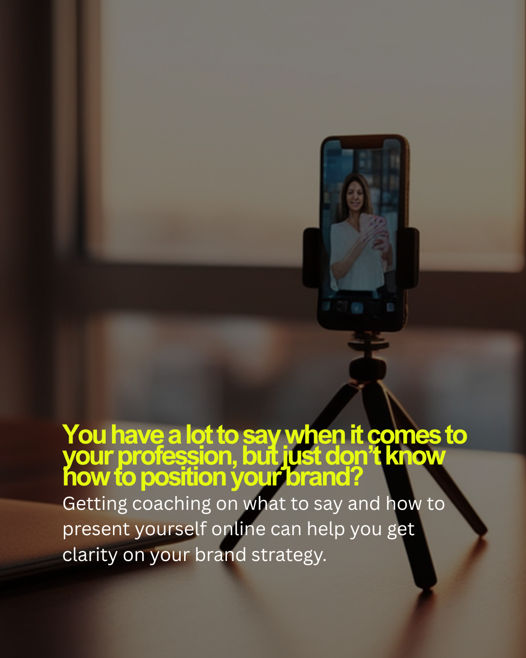 A smartphone mounted on a small tripod captures a woman smiling and taking a selfie. The background is blurred.