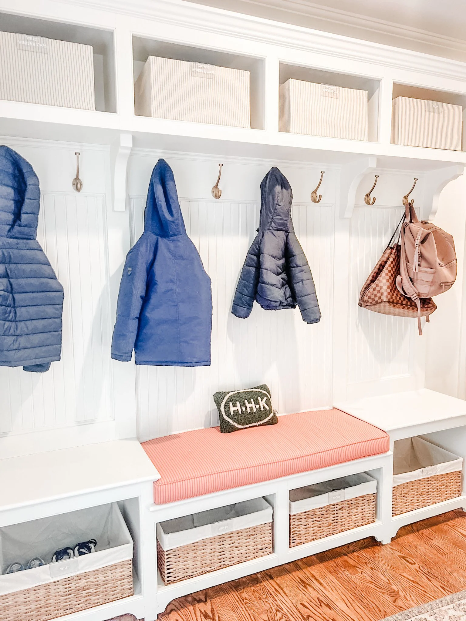 Entryway organization combines a bench, labeled baskets, hooks, and overhead bins for family storage.