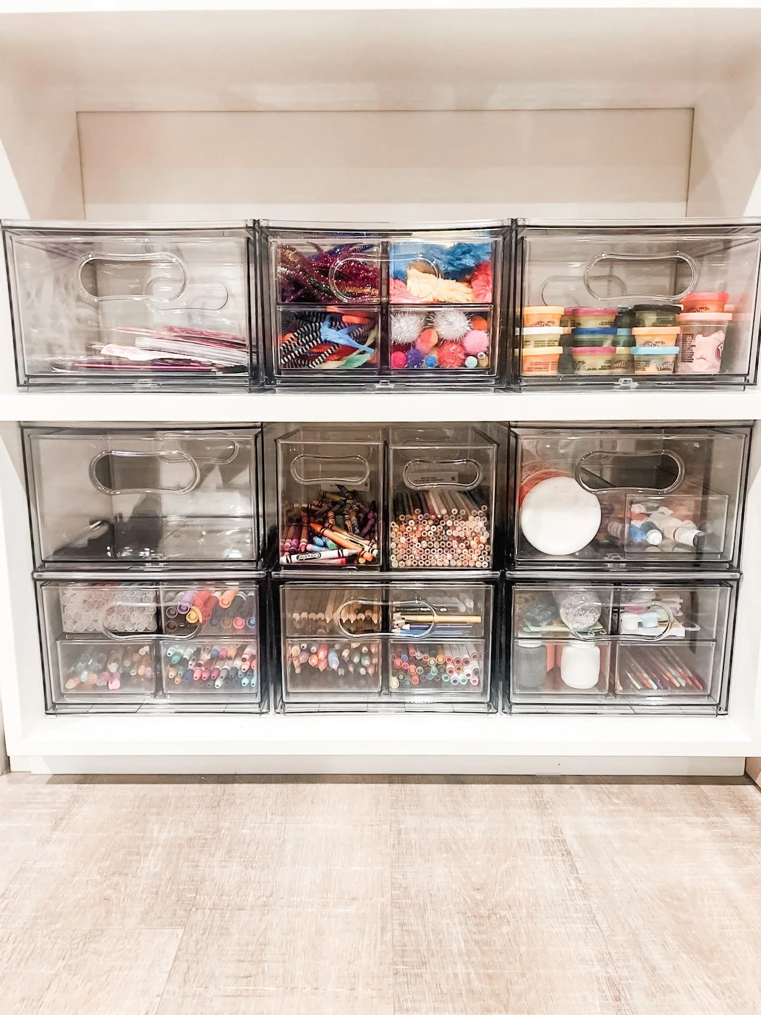 White shelving unit with clear modular drawers neatly sorted by a decluttering service, holding organized yarn, markers, and craft supplies.