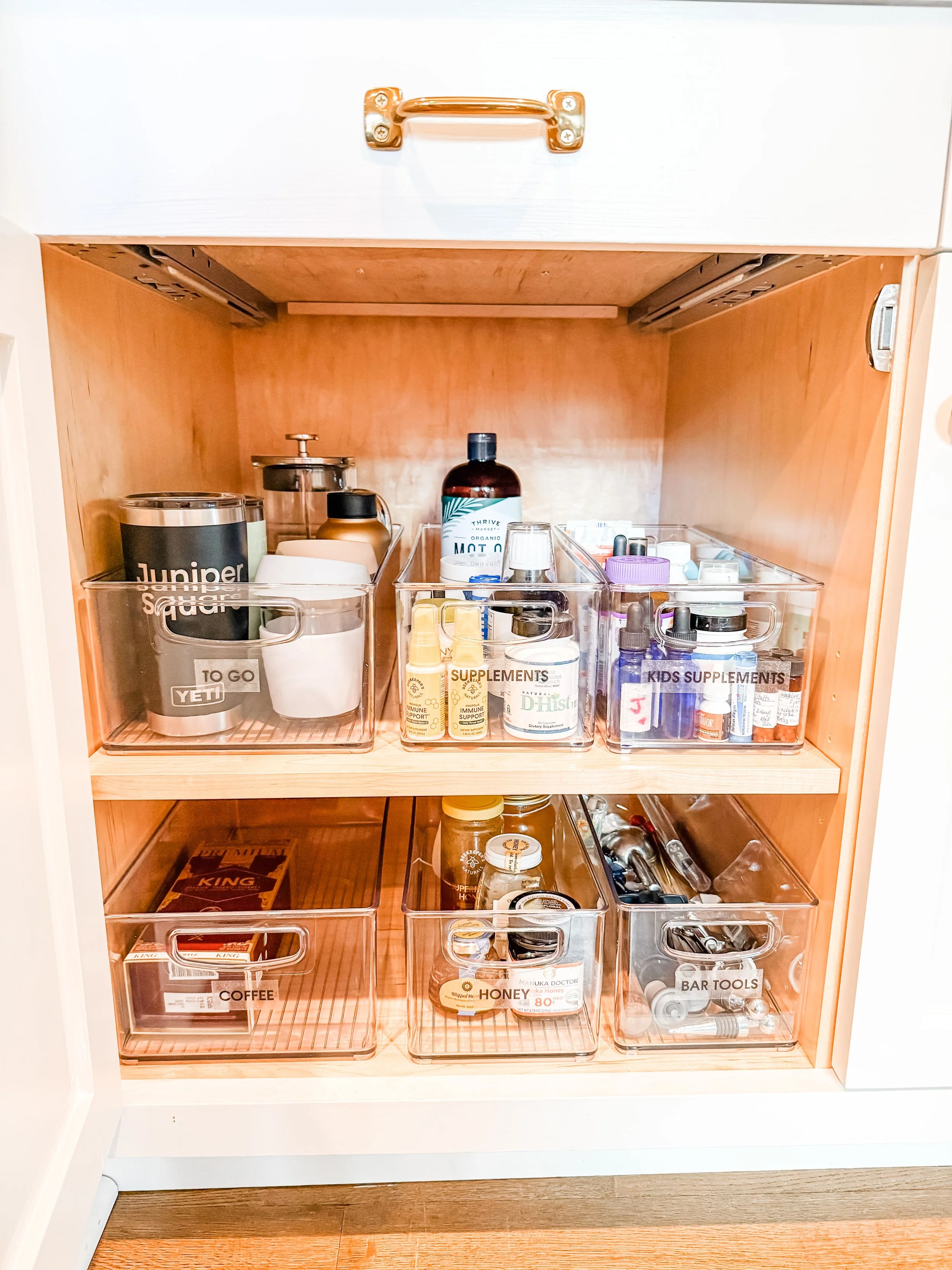Organized kitchen cabinet with labeled bins for coffee and supplements, featuring a Yeti mug, arranged by a professional decluttering service.