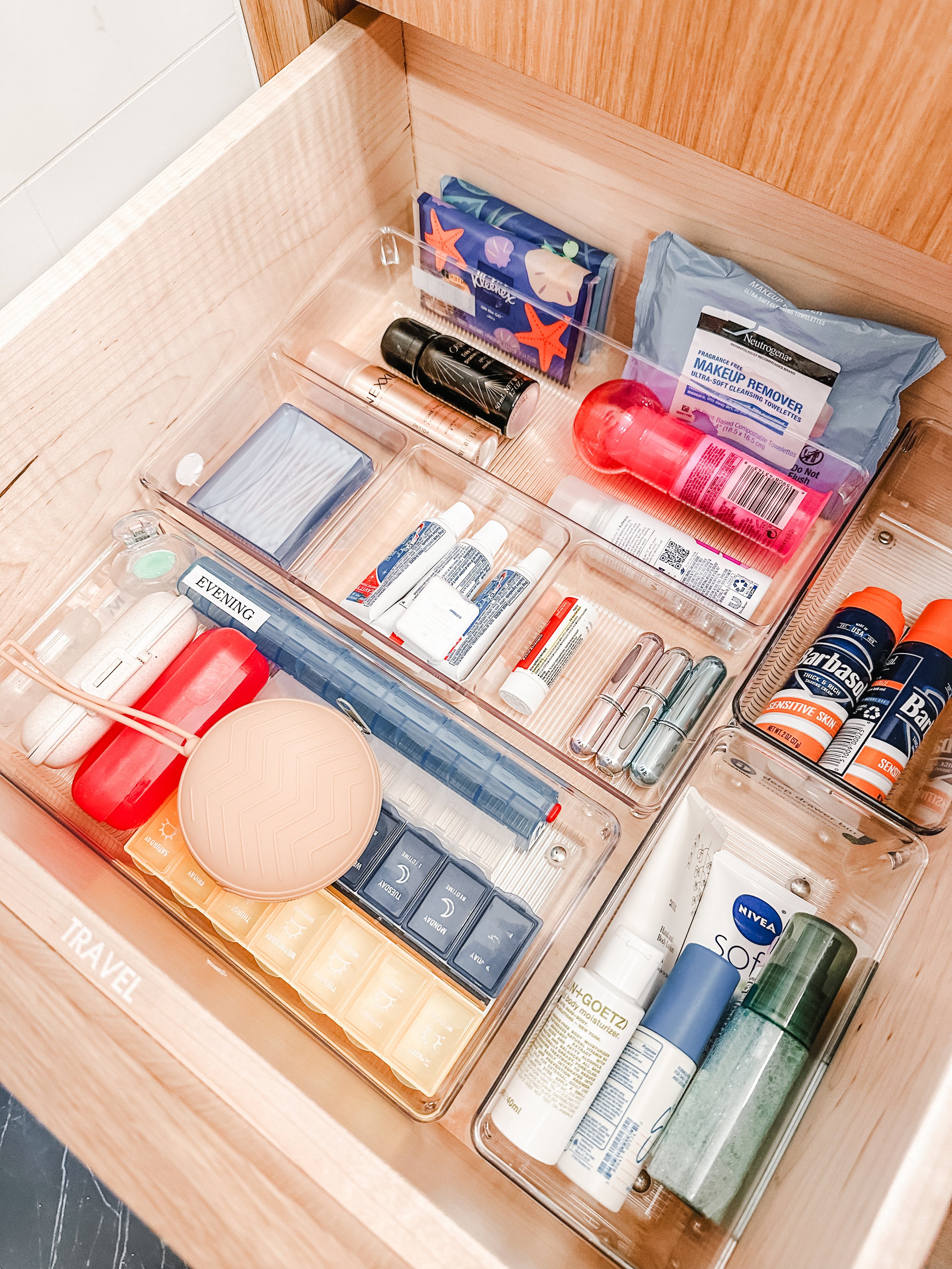 Clear acrylic bins neatly store travel toiletries in a drawer, showing professional home organization.